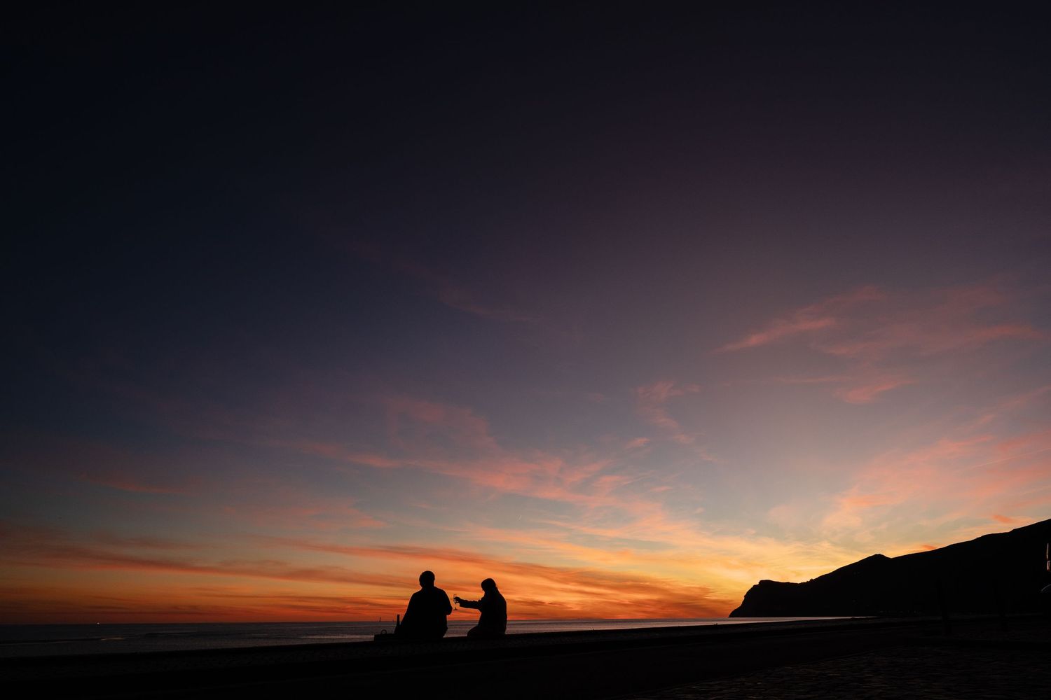Two people in white shirts sit close together on the ground at night in a series of intimate candid moments.