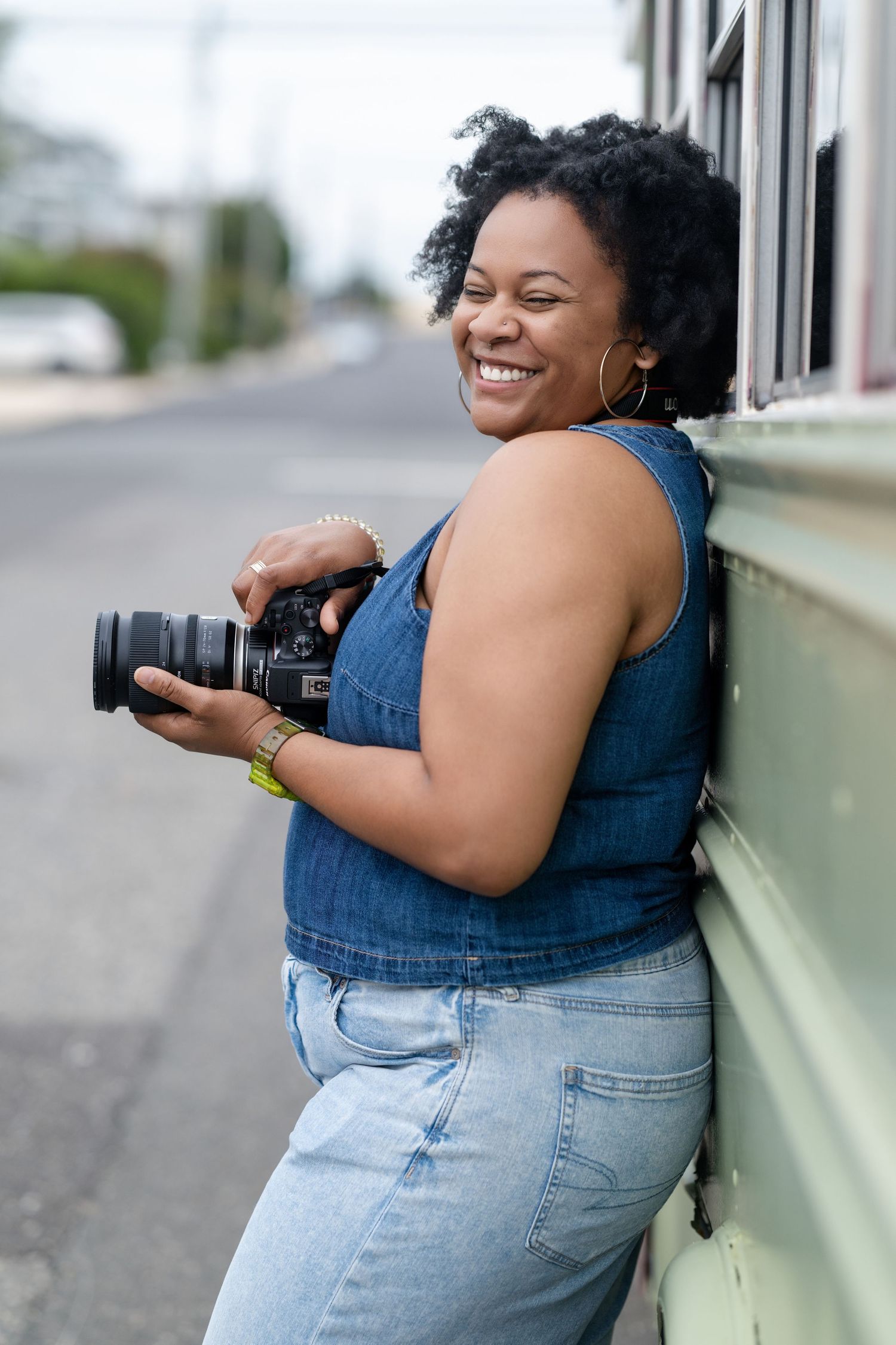 Photographer with camera smiling while leaning against light green bus exterior.