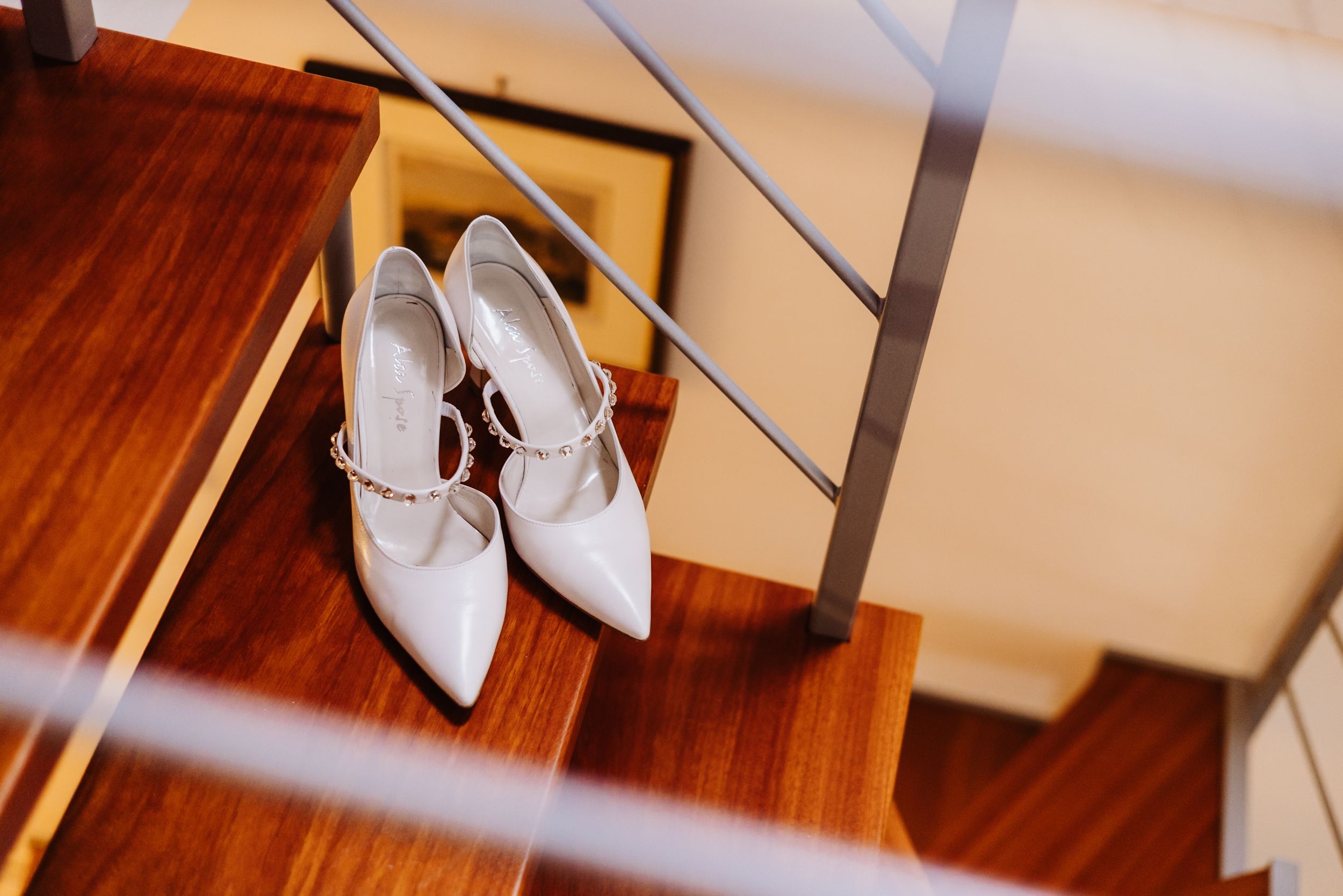 White leather wedding heels with ankle straps sit elegantly on a polished hardwood floor.