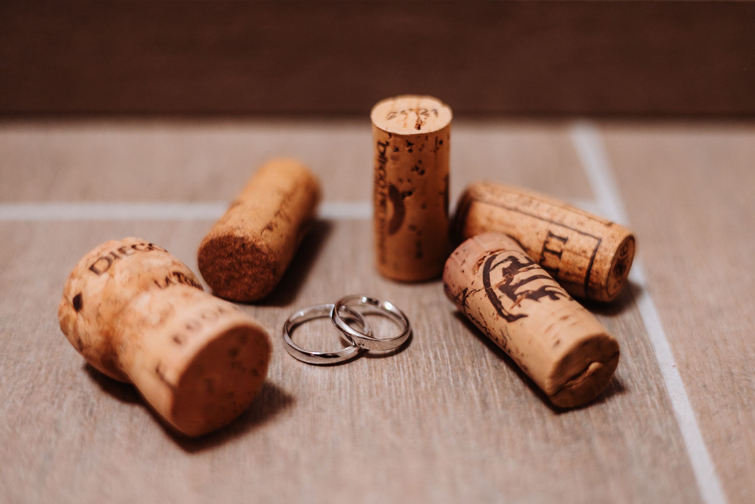 Wedding rings displayed among scattered wine corks on a rustic wooden surface in warm lighting.