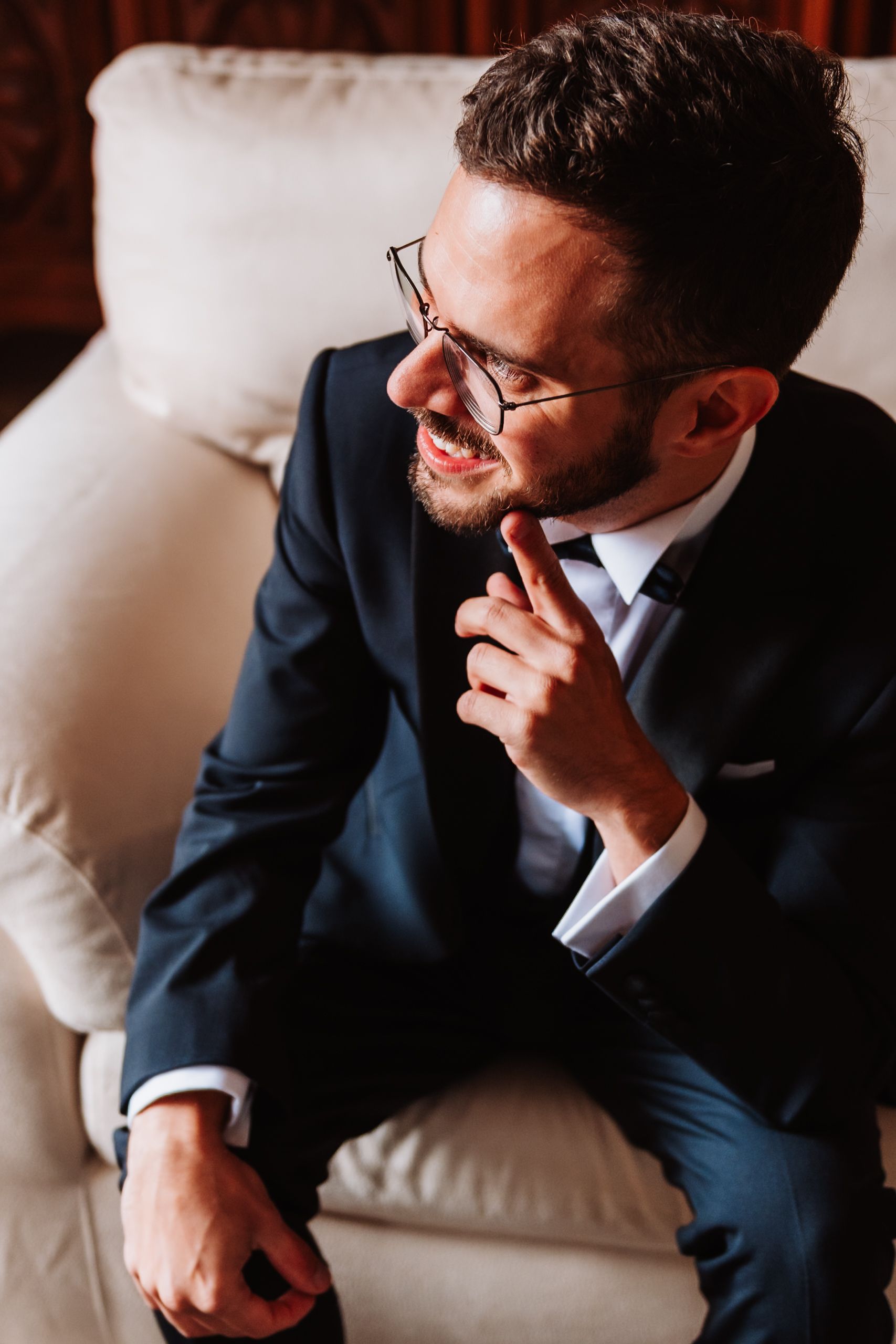 A person in a navy suit sits thoughtfully on a white couch, photographed from multiple angles in warm lighting.