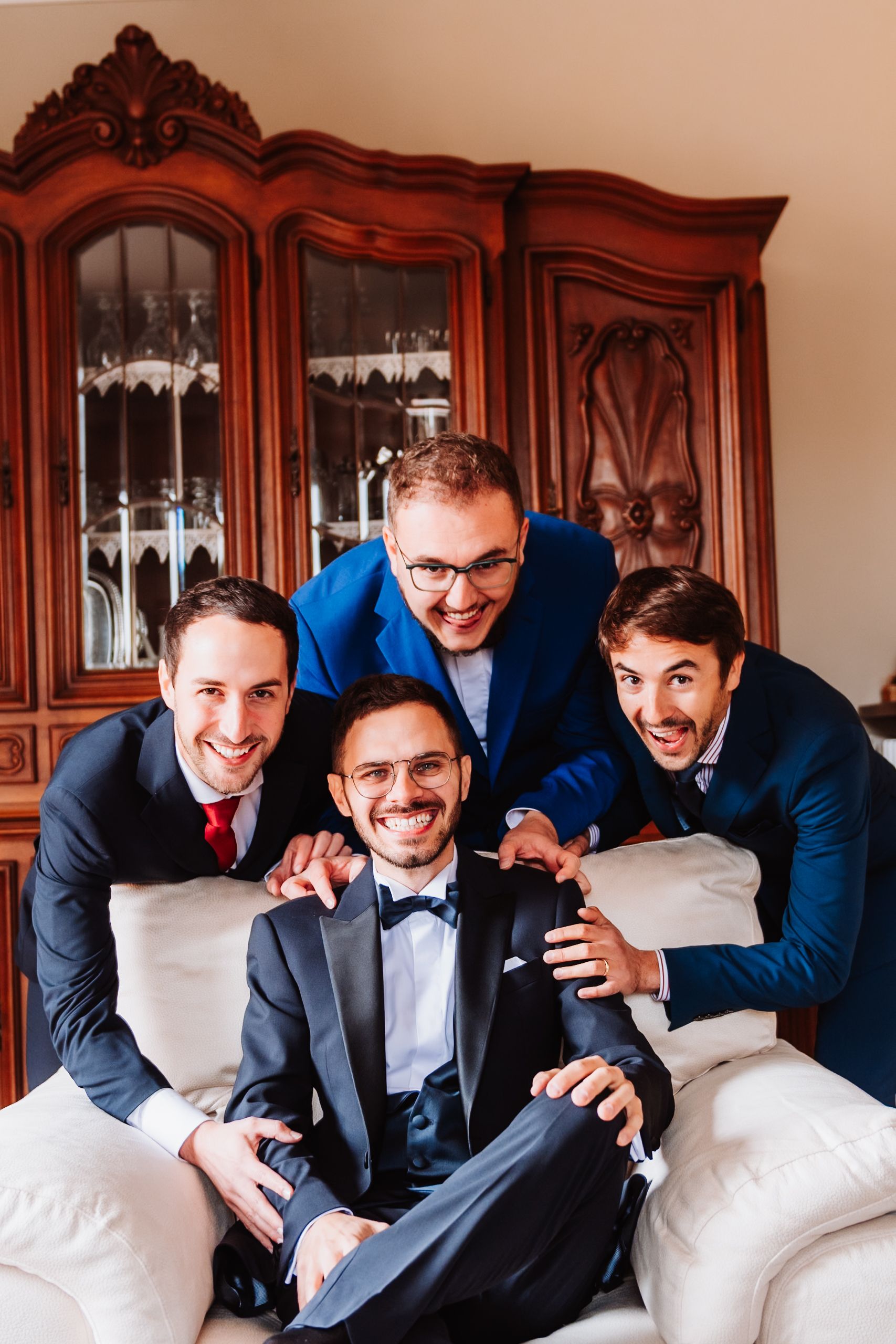 Groomsmen in navy suits pose playfully on white couch in sequence of progressive photos.
