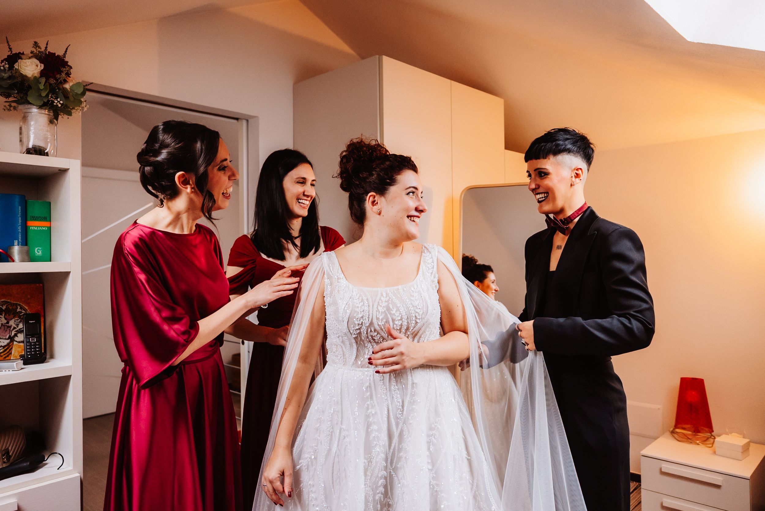 A wedding party getting ready in a bright indoor space with burgundy and white attire.