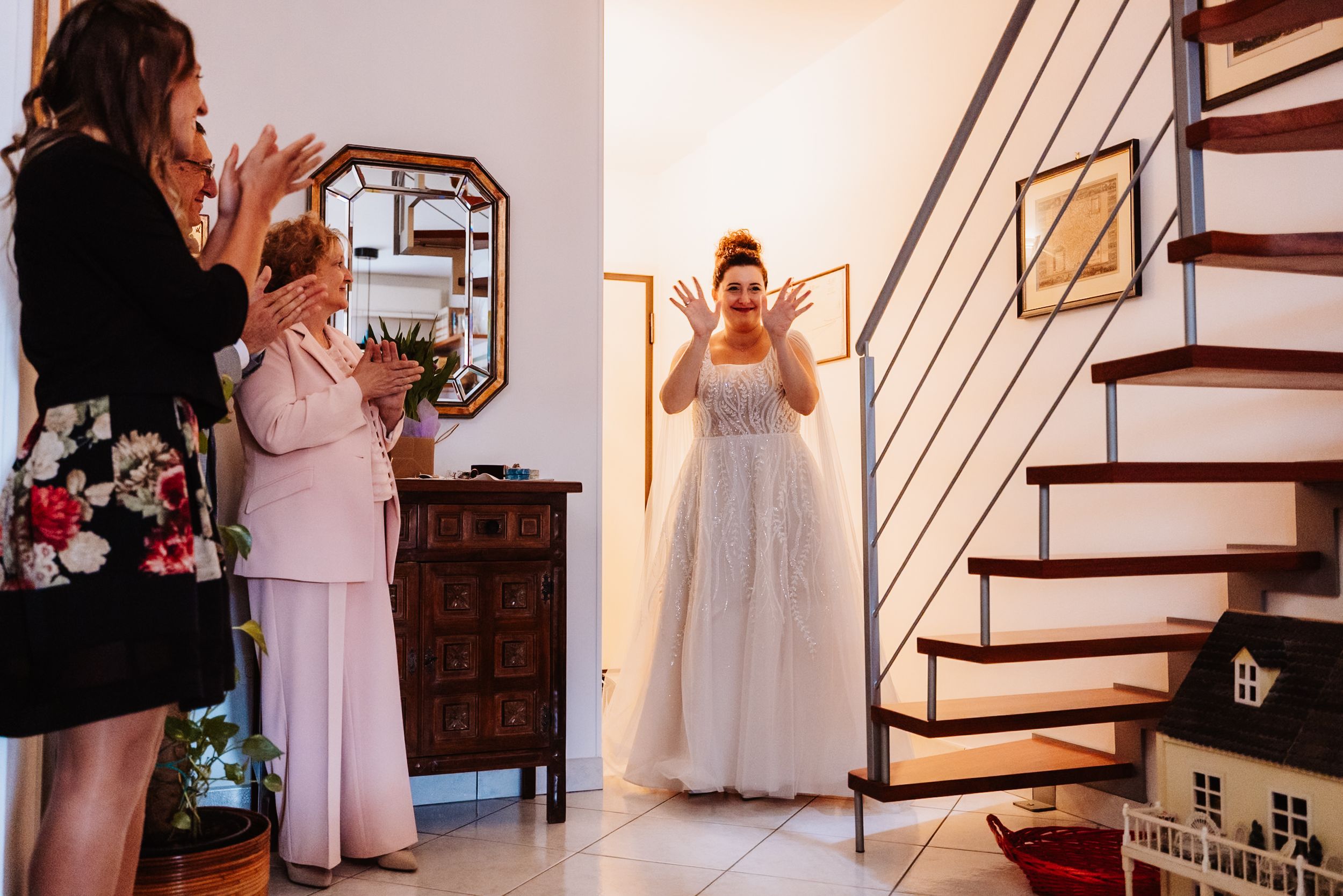 Bride in white wedding dress stands in front of a wooden staircase while getting ready for her wedding ceremony.