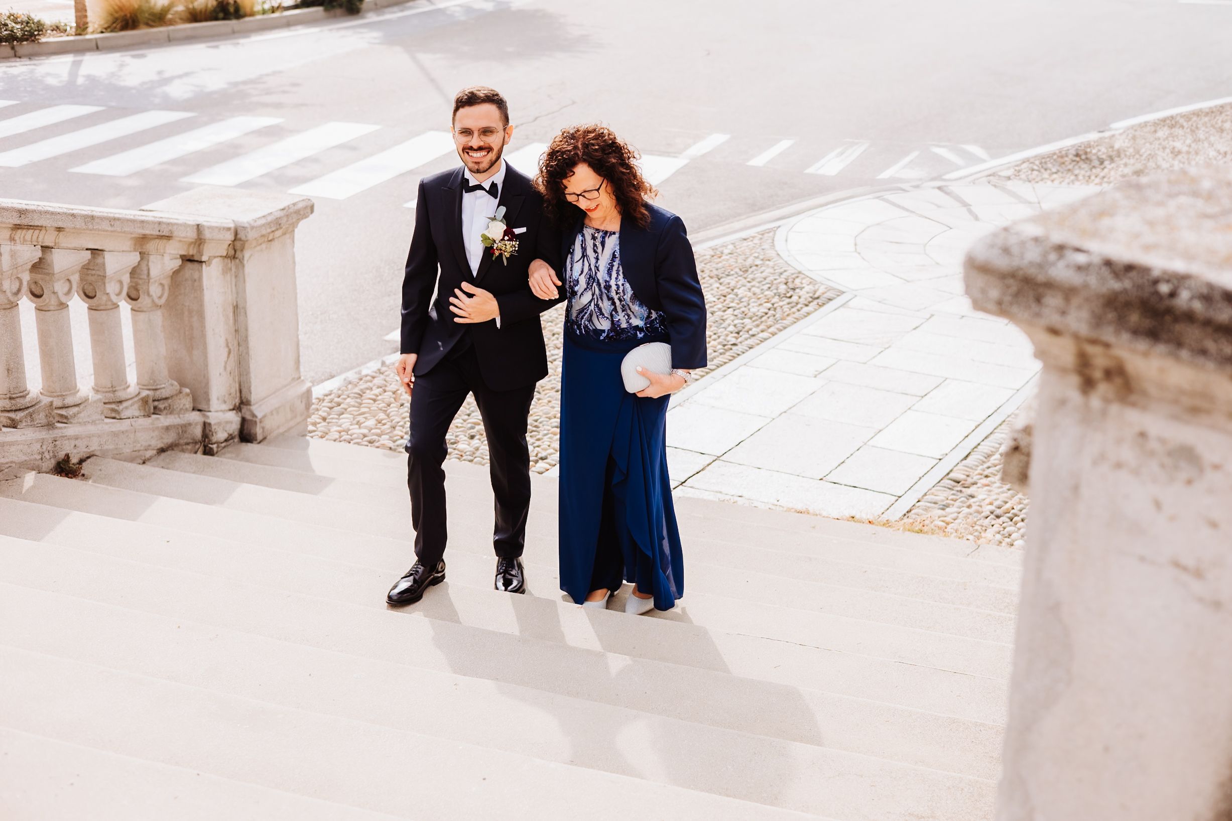 Two people walk down historic stone steps in formal attire during a photoshoot.