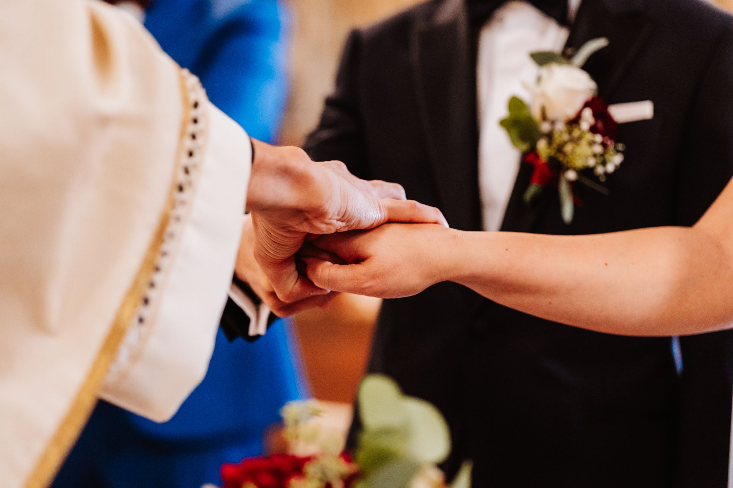 Close-up of hands exchanging wedding rings during a traditional ceremony with white and gold decor in background.