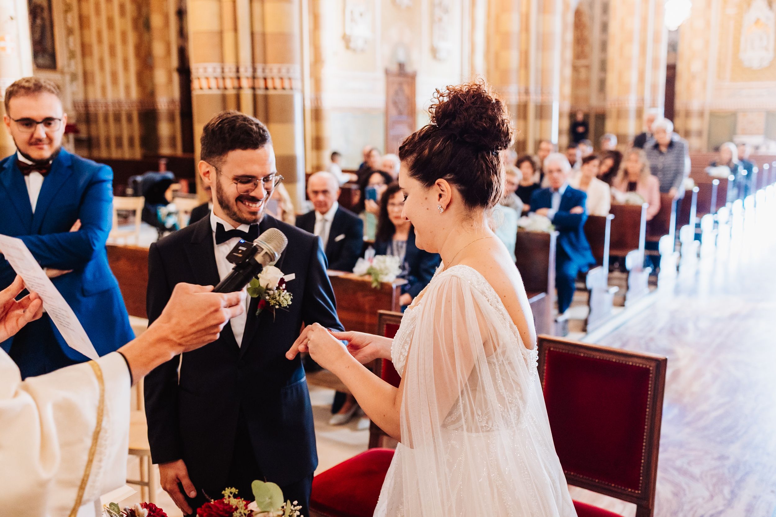Wedding ceremony guests gathered in an elegant church interior with ornate architectural details.