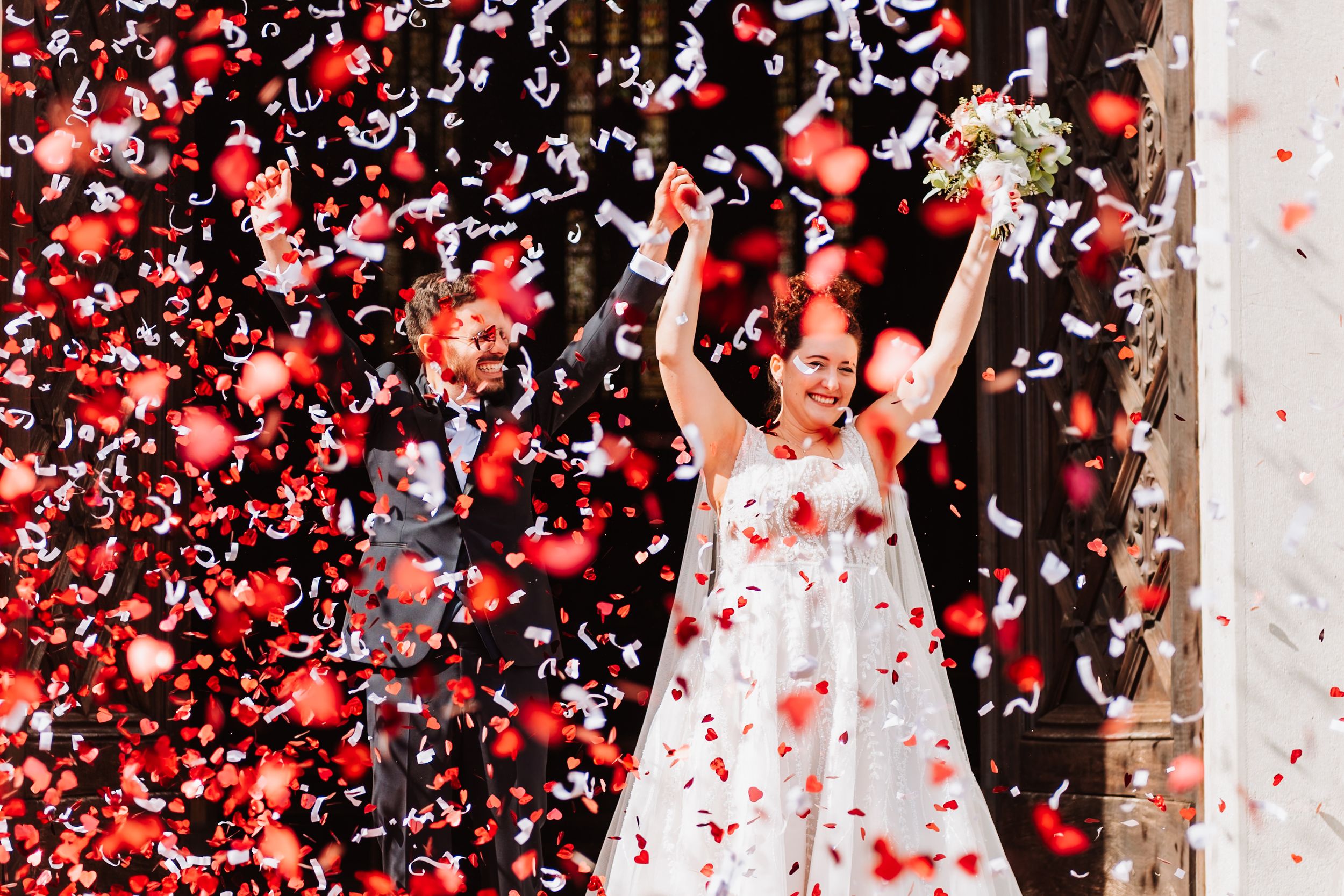 Confetti and rose petals shower down on a celebratory wedding scene with white decor and joyful atmosphere.
