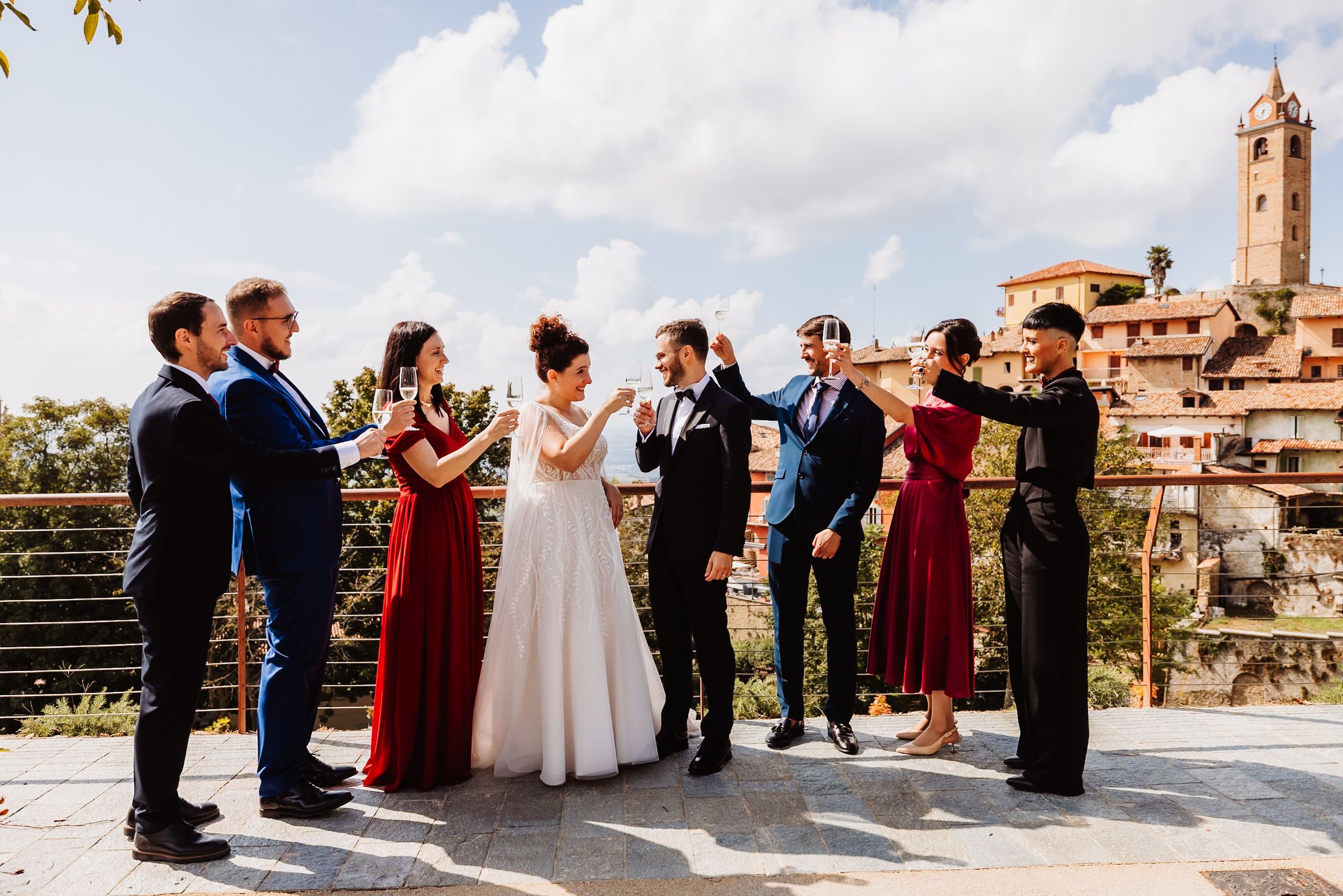 Wedding party stands in line on a sunny terrace with views of an Italian village and church tower in background.
