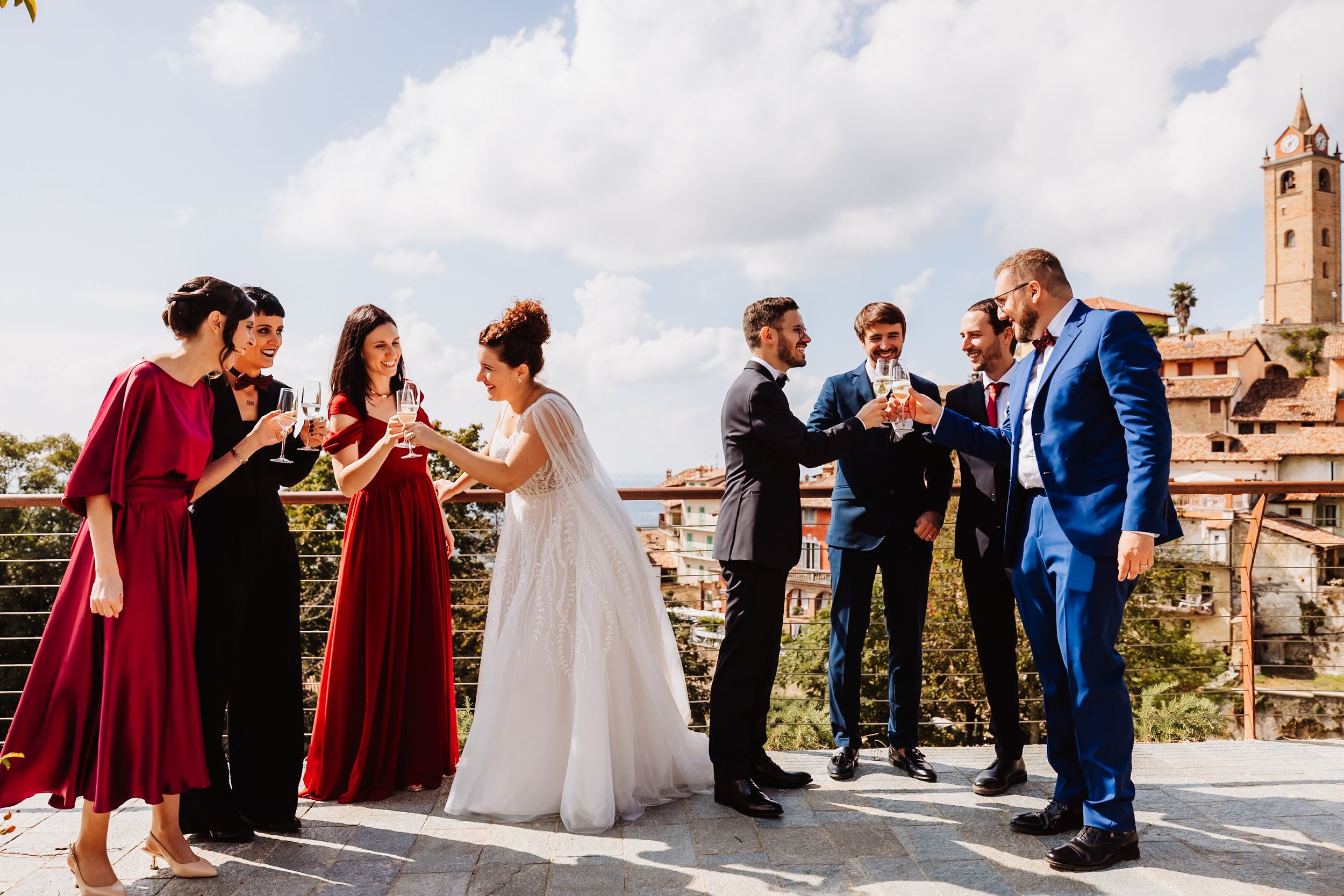 Wedding party in burgundy dresses and blue suits poses against scenic Mediterranean backdrop.