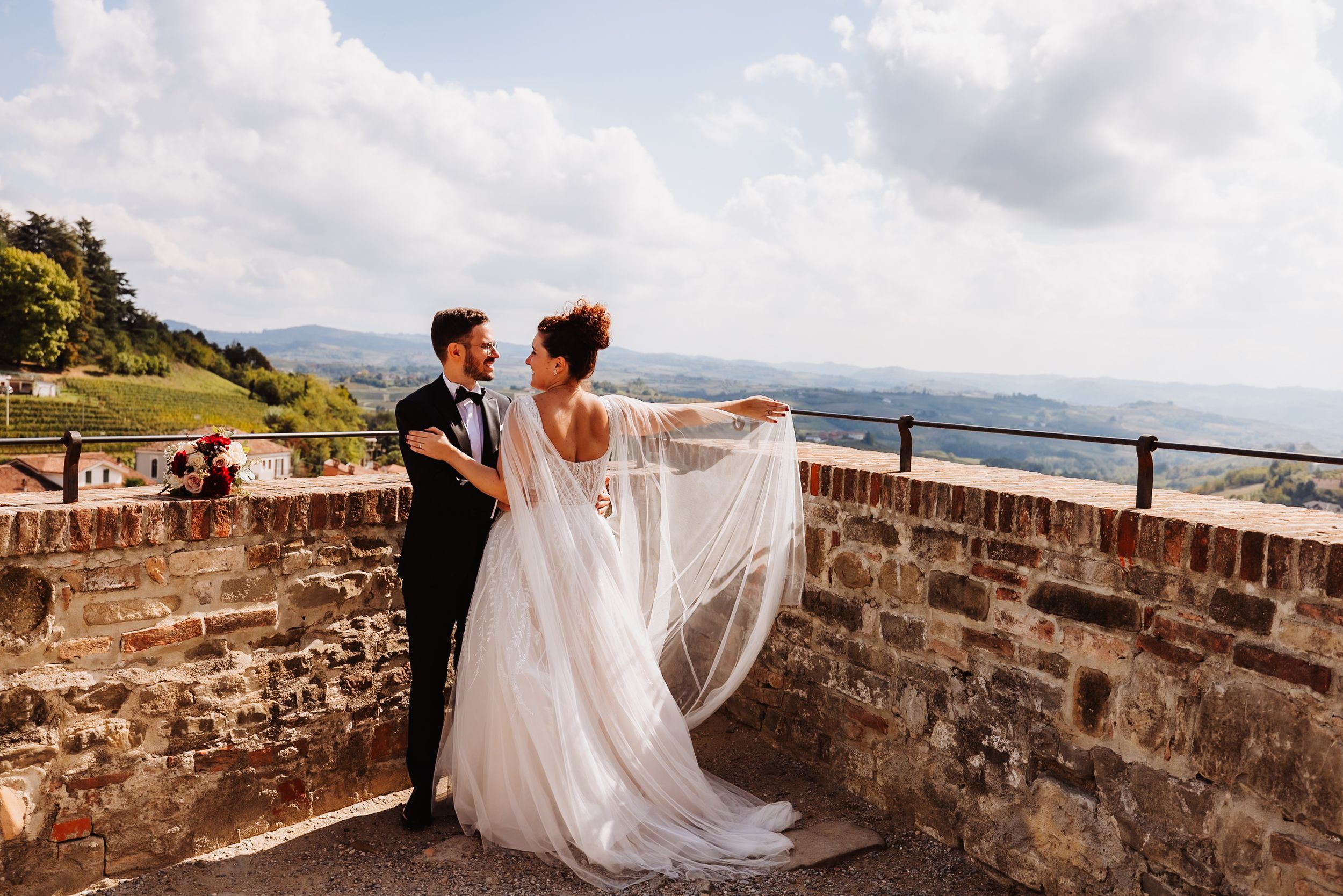 Couple in wedding attire photographed along scenic stone walls overlooking coastal landscape views.