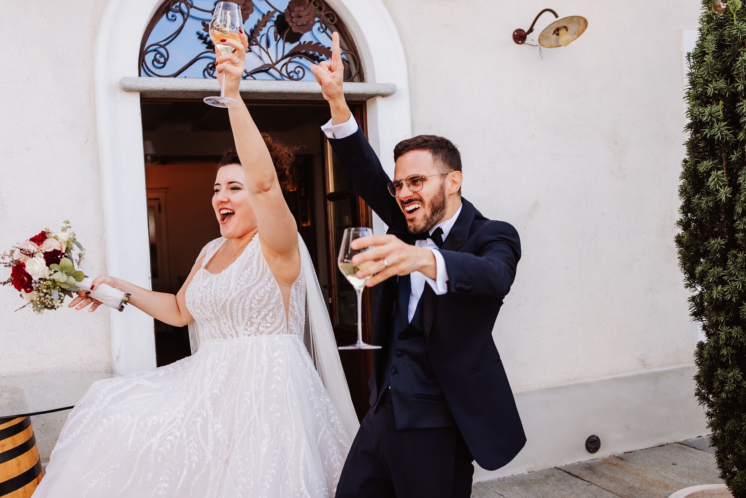 Joyful couple celebrating at their wedding ceremony with confetti flying in the air outside a white building.