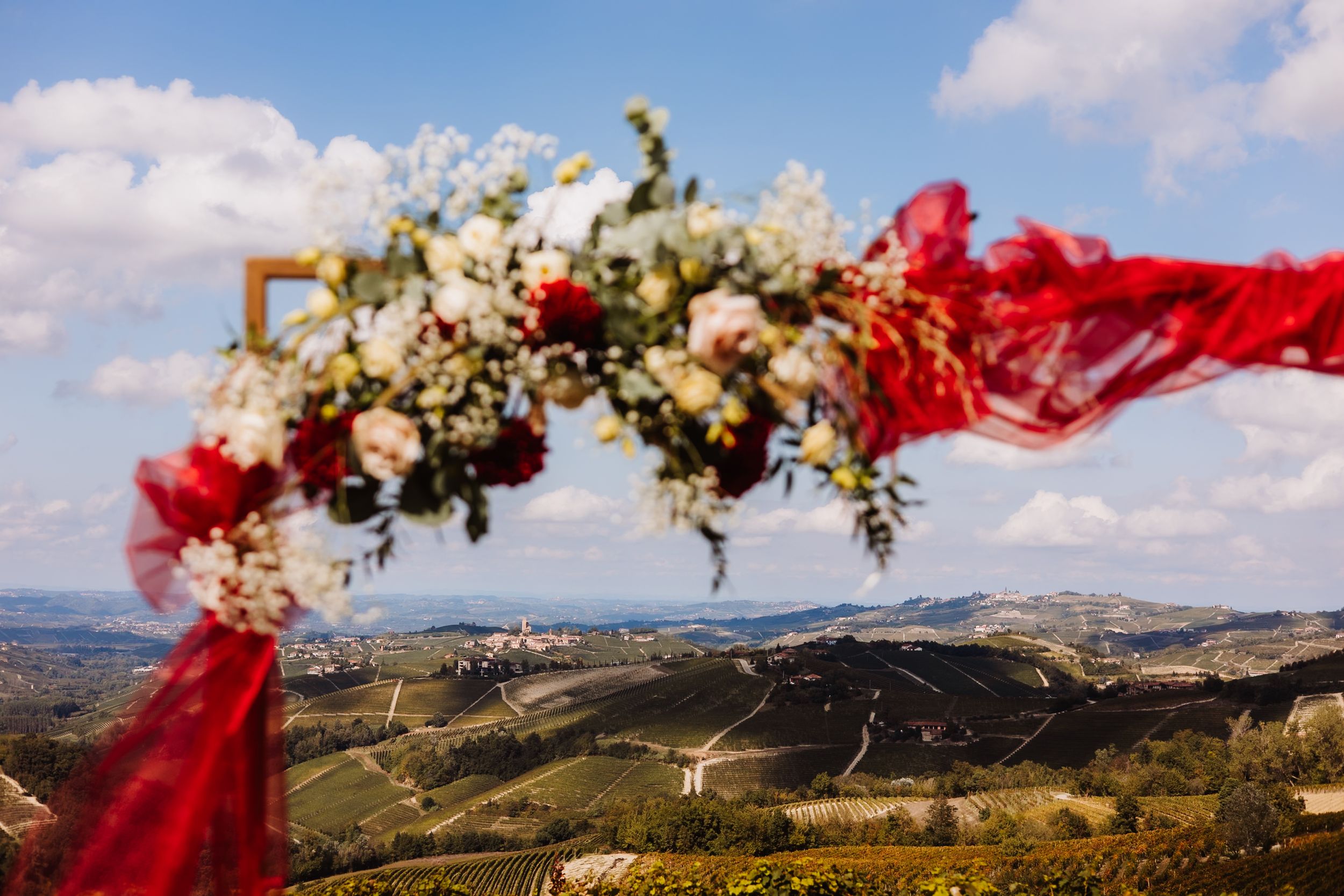 A panoramic mountain landscape with red fabric flowing in the wind against a cloudy blue sky.