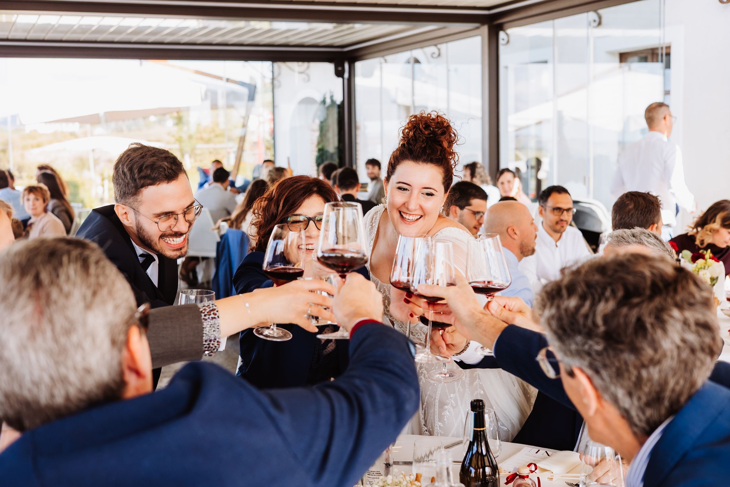 Wedding guests raise their glasses in a celebratory toast during a reception at an indoor venue.