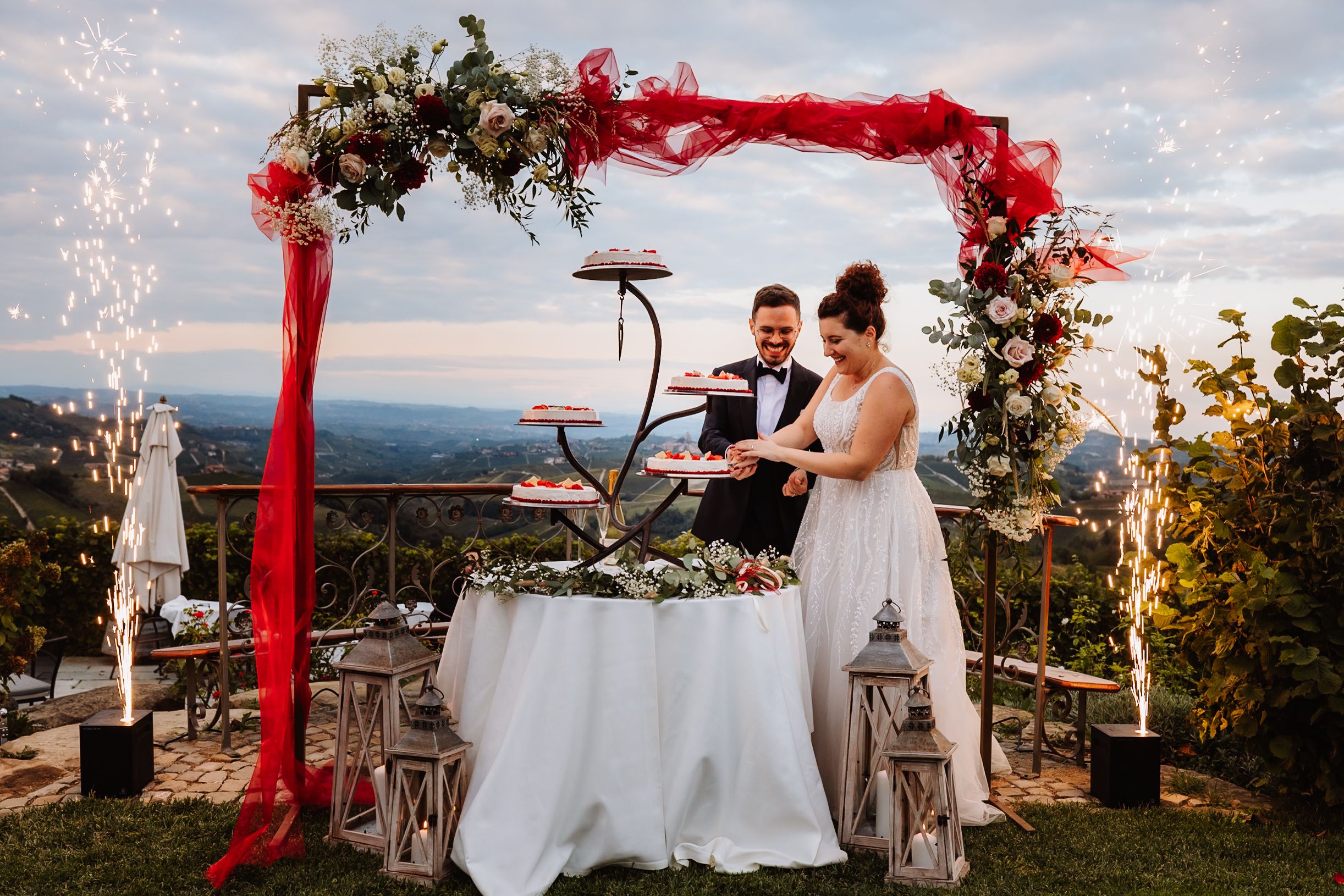 Elegant wedding ceremony setup on a mountain overlook with flowing red fabric draping and white table linens at sunset.