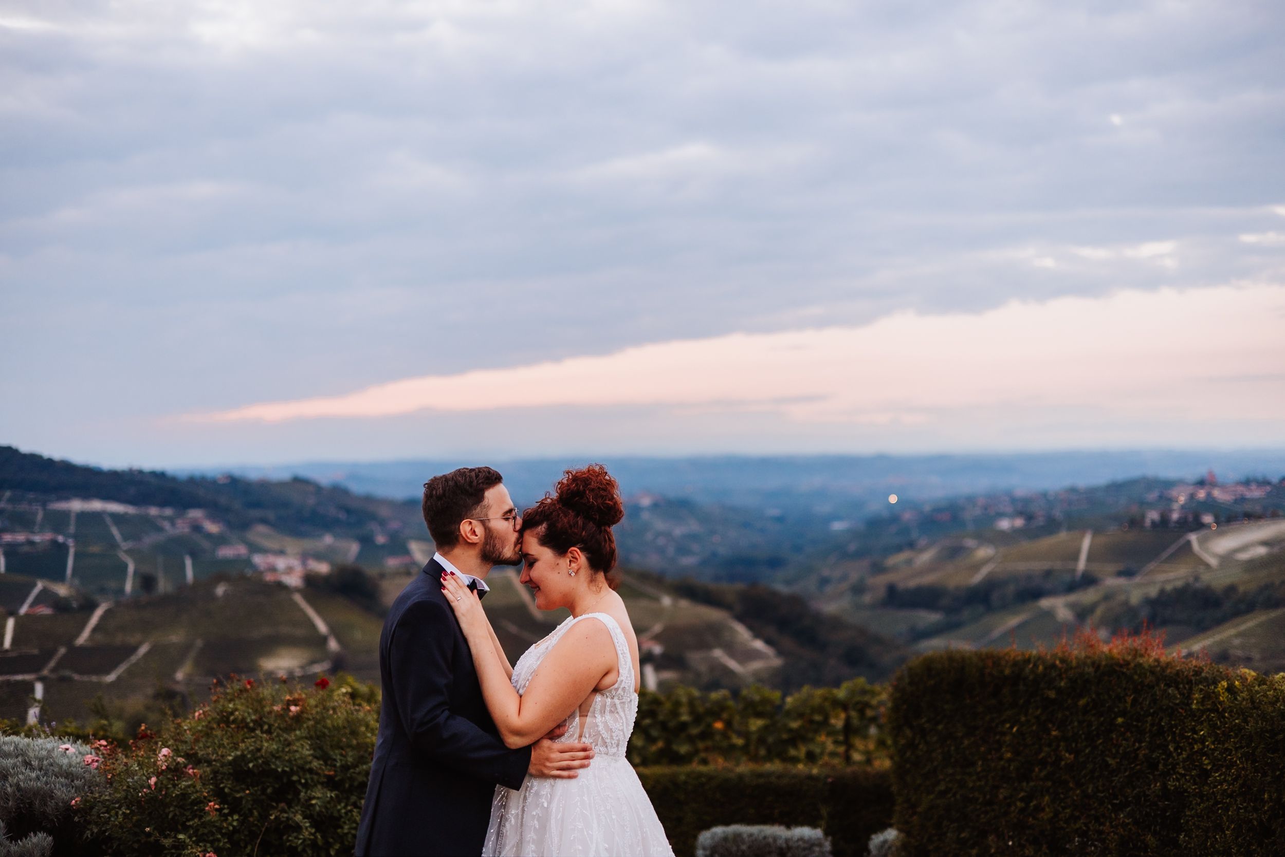 Two people share a romantic moment at sunset overlooking a scenic mountain vista.