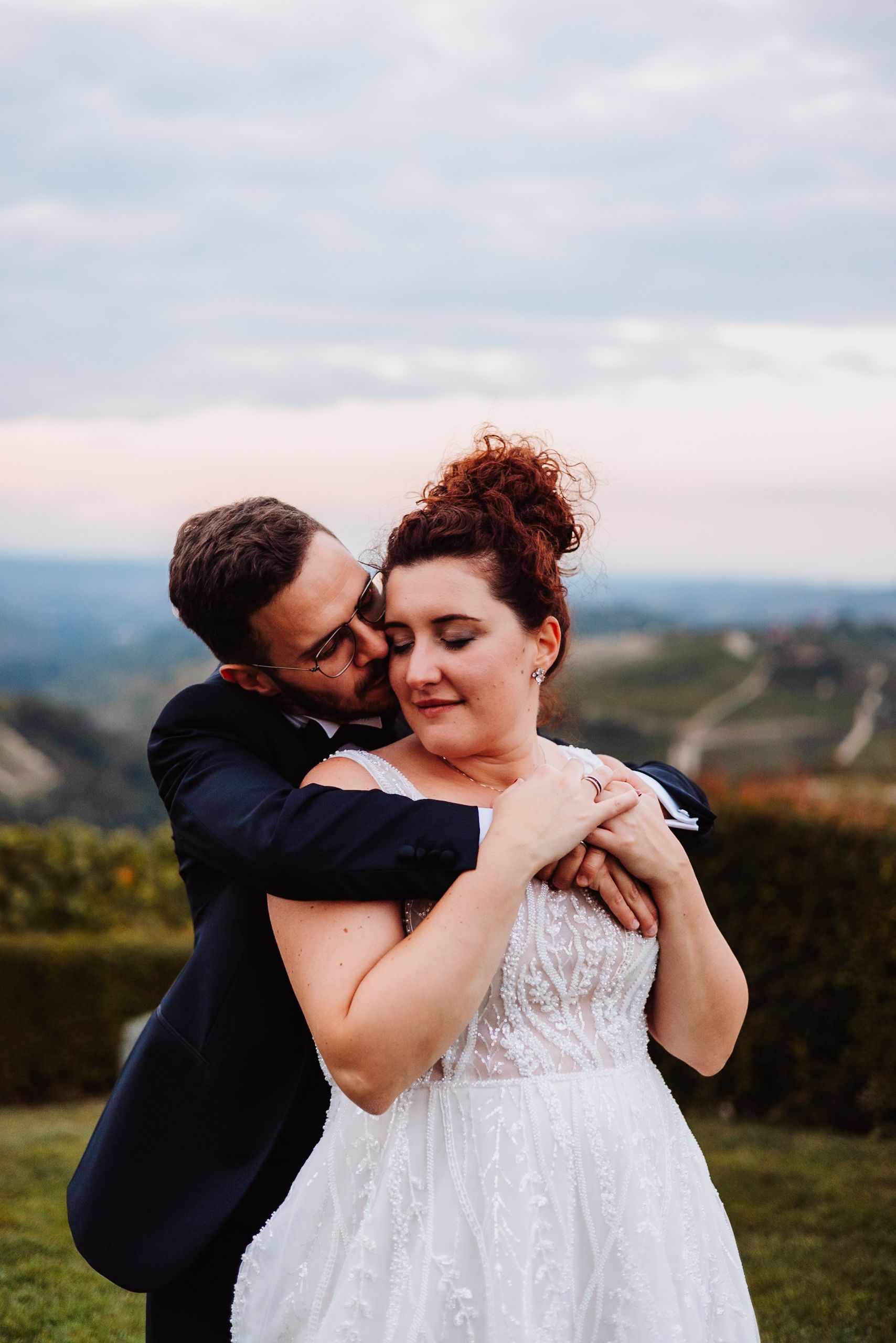 A romantic wedding couple shares tender moments on a hilltop overlooking a scenic countryside landscape.