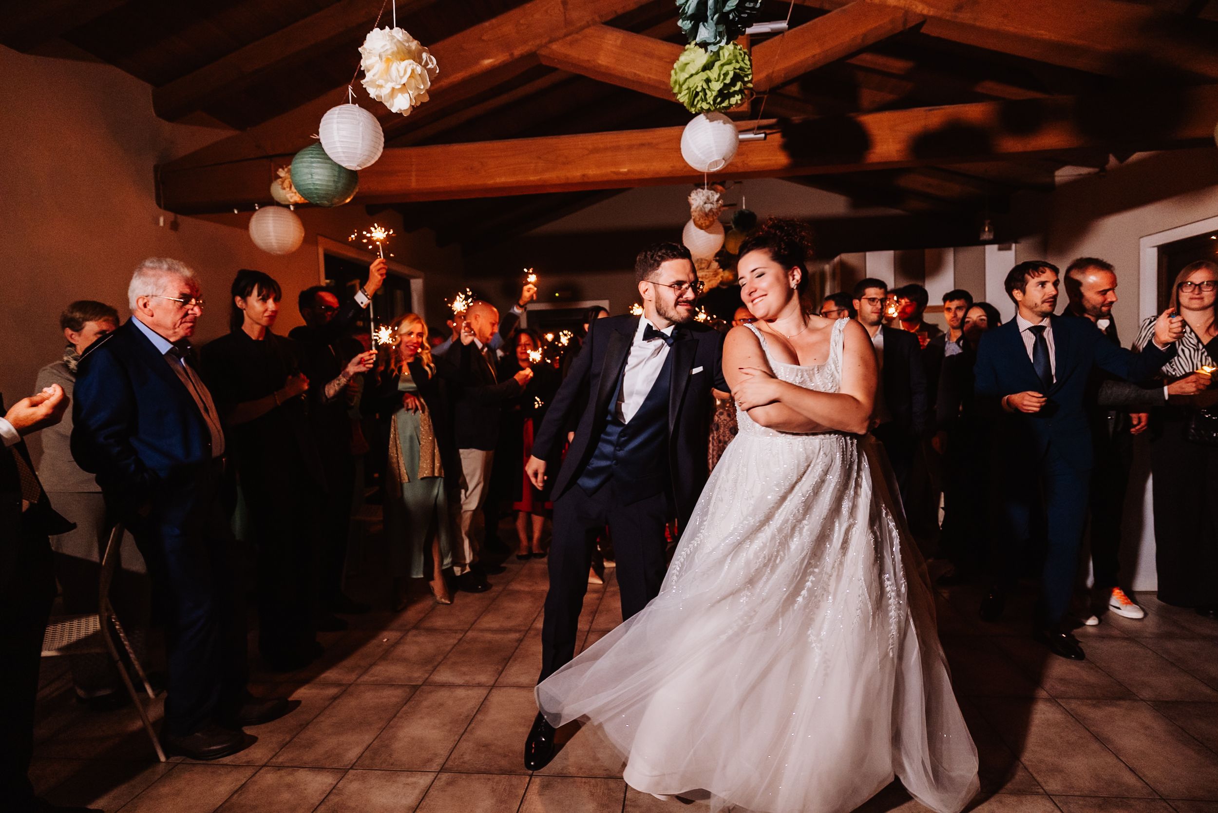 Wedding guests dance and celebrate on a dimly lit dance floor during an evening reception celebration.