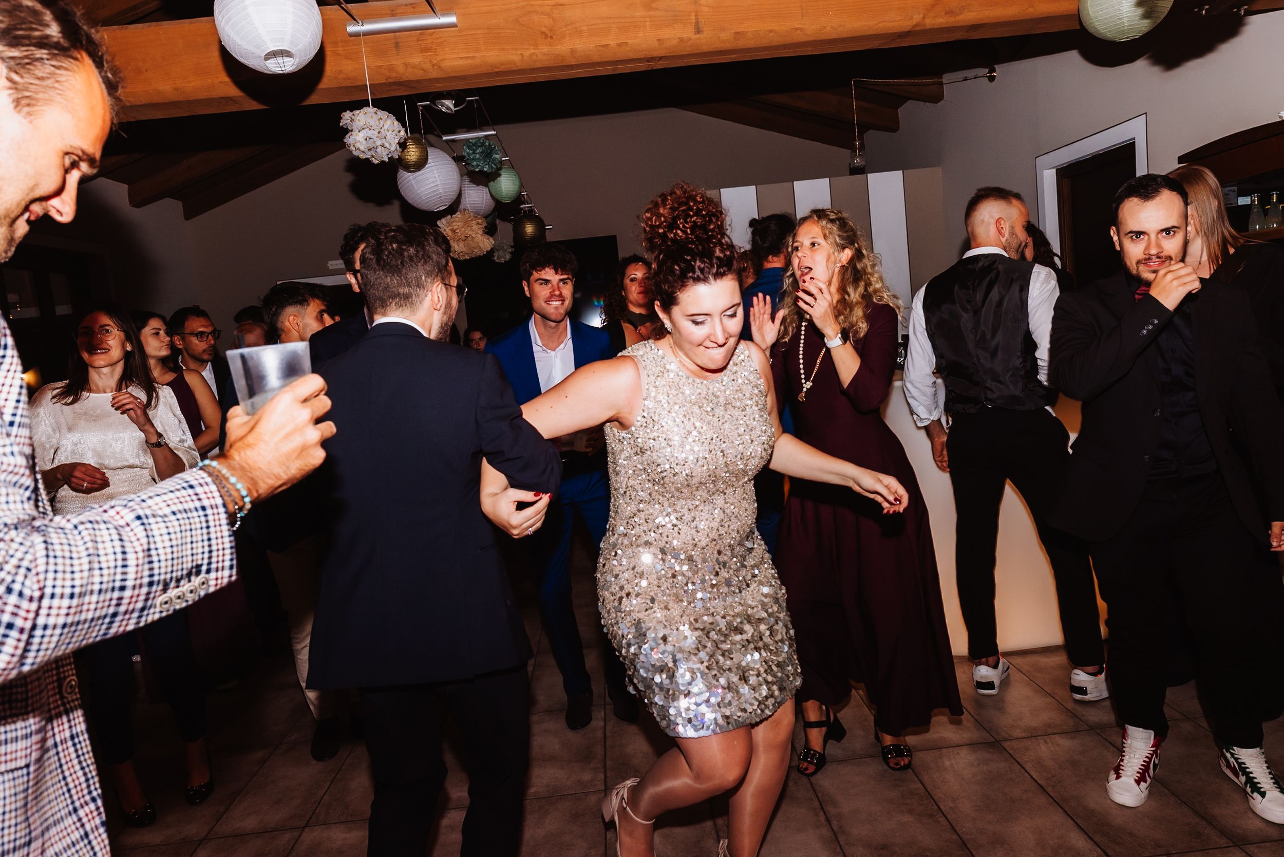 People dancing and socializing at a lively party or wedding reception in a dark indoor venue.