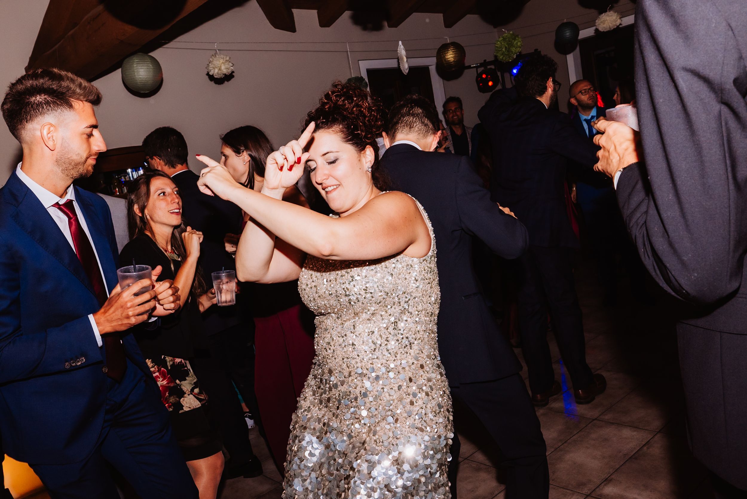 Wedding reception guests dance and celebrate on a dimly lit dance floor at an evening celebration.