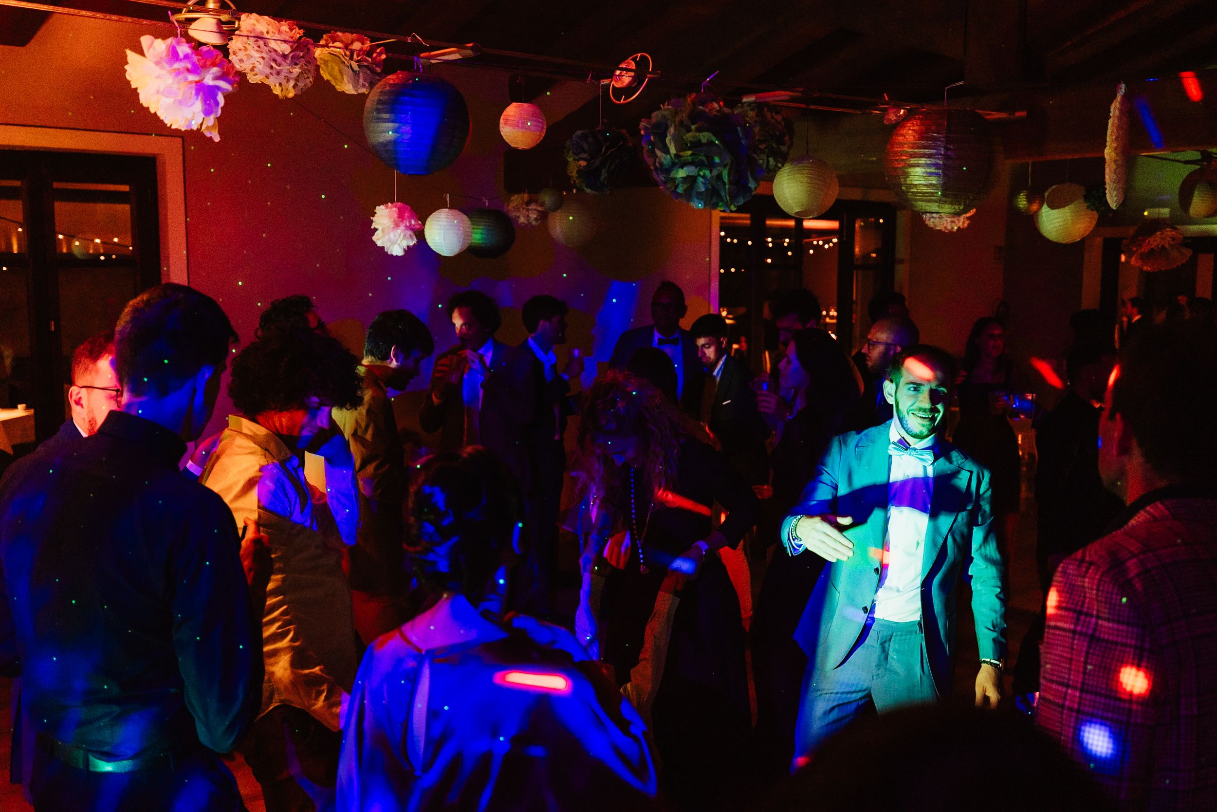 People dancing at a nightclub with colorful blue lighting and paper lantern decorations hanging from the ceiling.