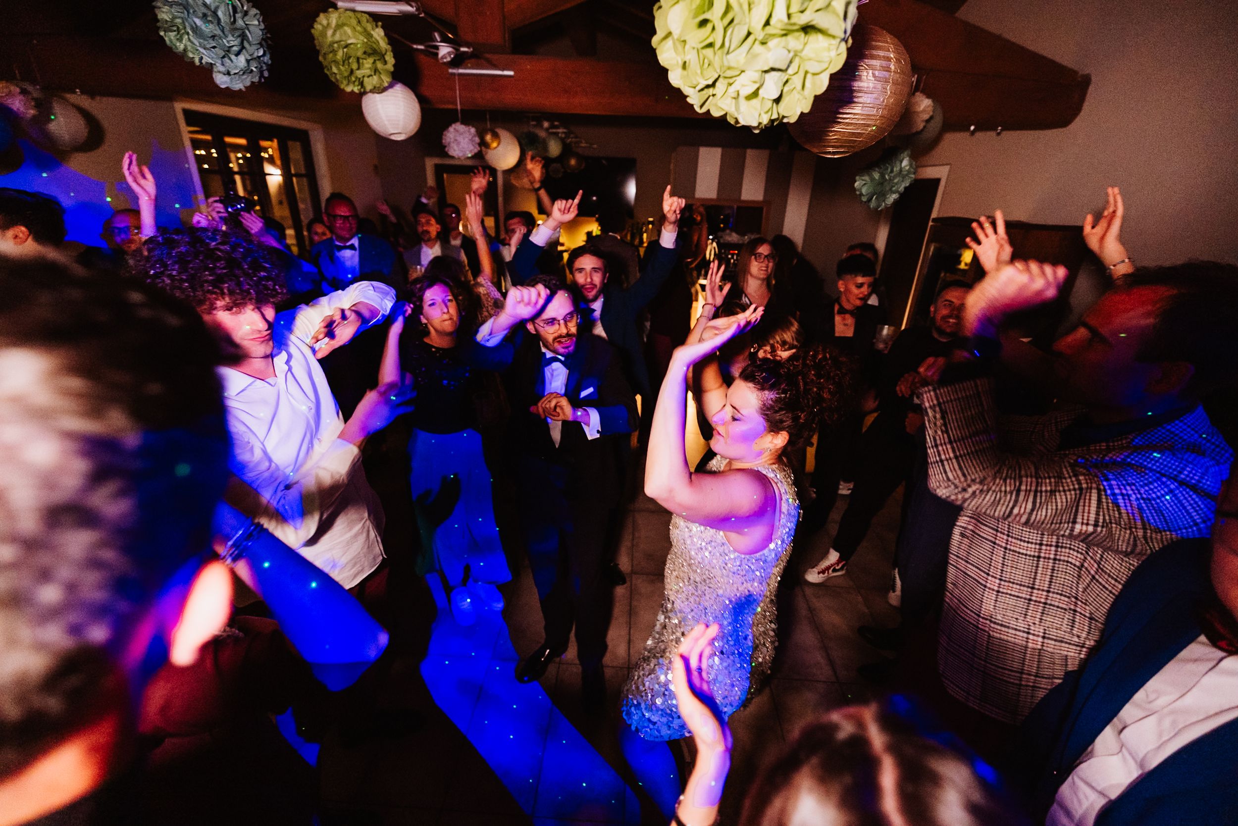 Crowded dance floor illuminated by blue lights at a nightclub party with people dancing and celebrating.