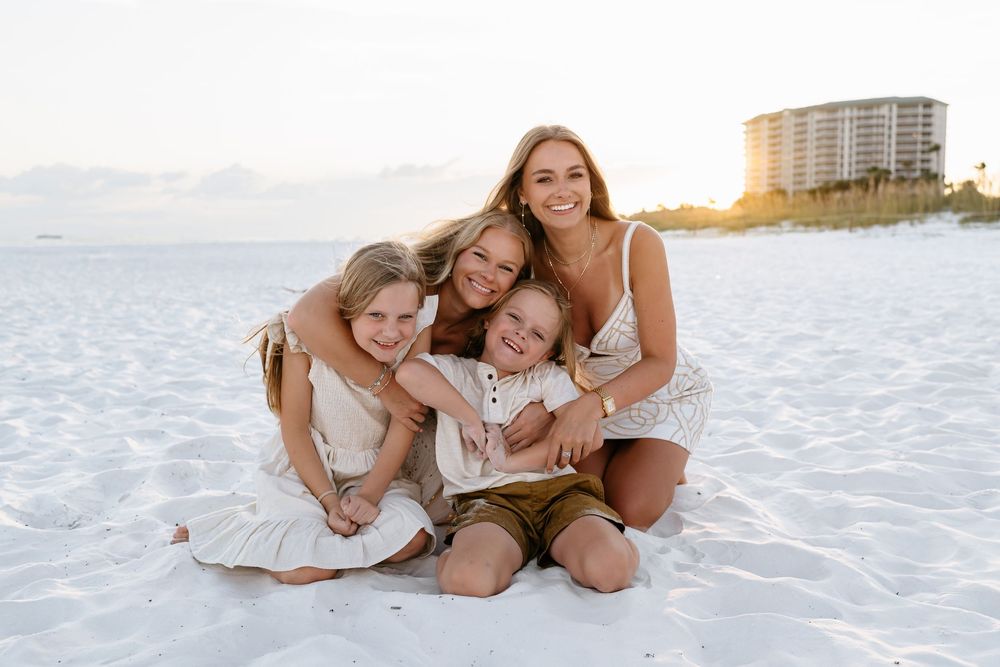 A loving family wearing white outfits poses together on a pristine beach at sunset.