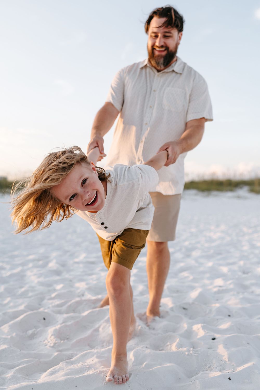 Playful beach scene showing someone being swung and spun around on white sand at sunset.