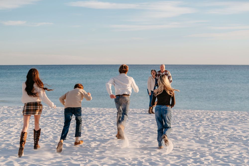 A group of friends running together on a white sandy beach with turquoise ocean waters in the background.
