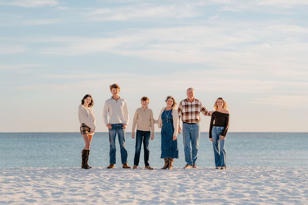 Group of people standing together on a white sandy beach at sunset with ocean views in the background.