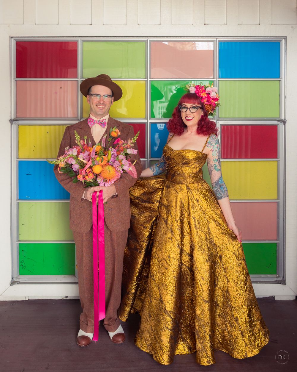 A couple poses in vintage-style attire against a colorful stained glass window backdrop at a retro photo shoot.
