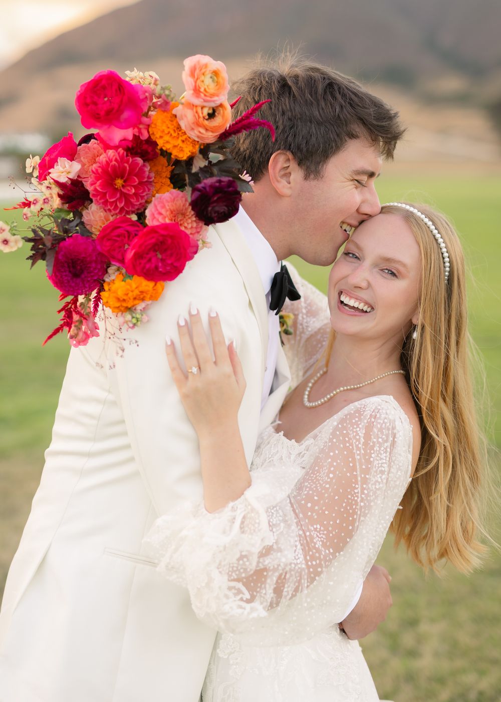 A romantic wedding moment with vibrant pink and orange florals against a mountainous backdrop.