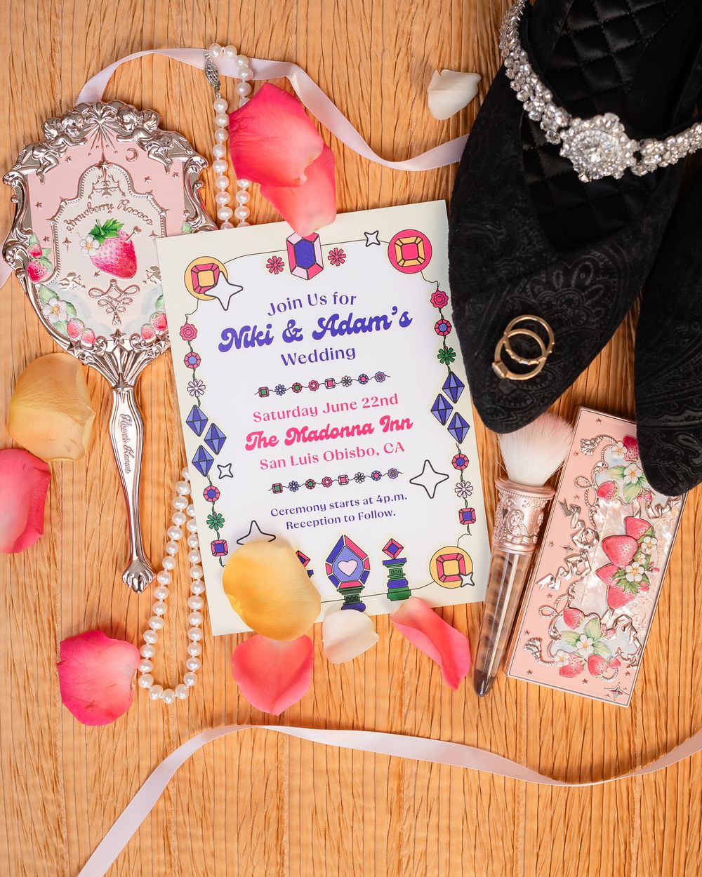 Wedding details including invitations, jewelry, and floral petals arranged on wooden surface.