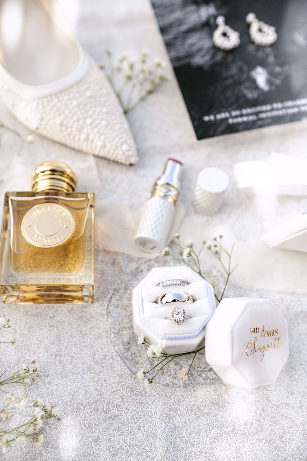 Luxury perfume bottles and wedding details arranged on a shimmering silver surface.