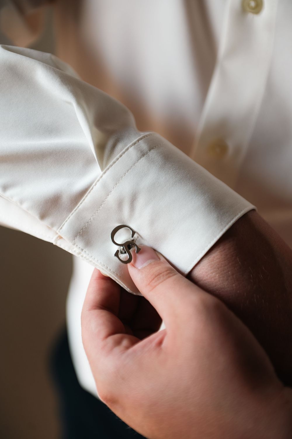 Close-up detail of cufflinks being fastened on a white dress shirt.