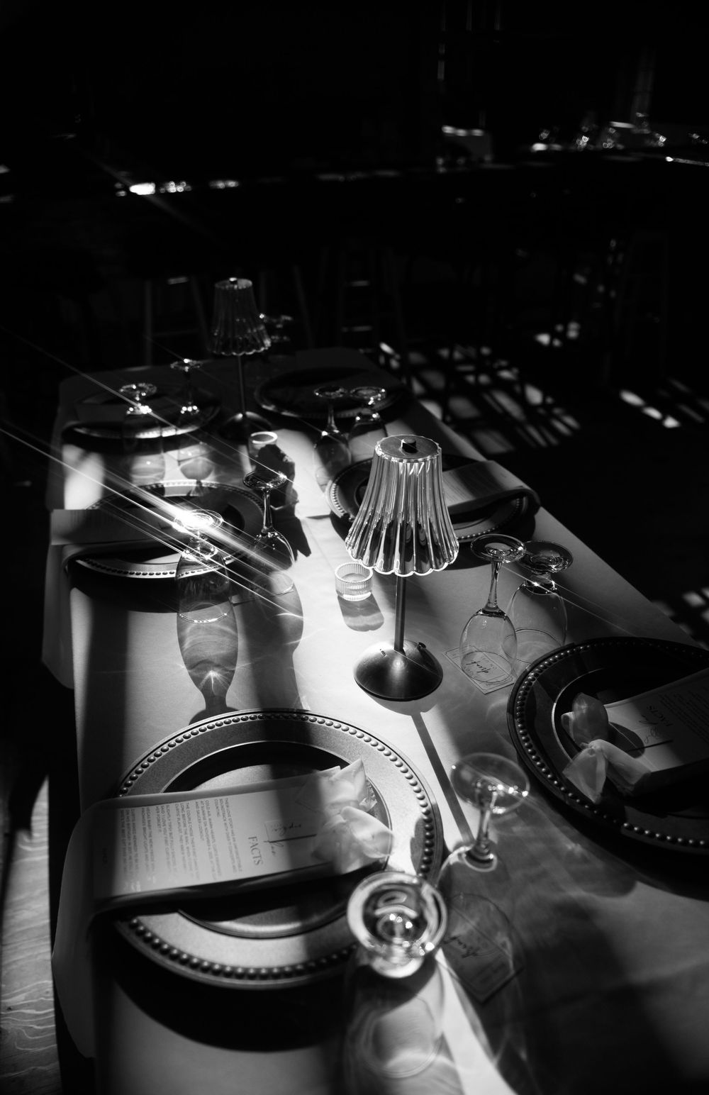 Black and white photo of wedding reception table settings with dramatic shadows.