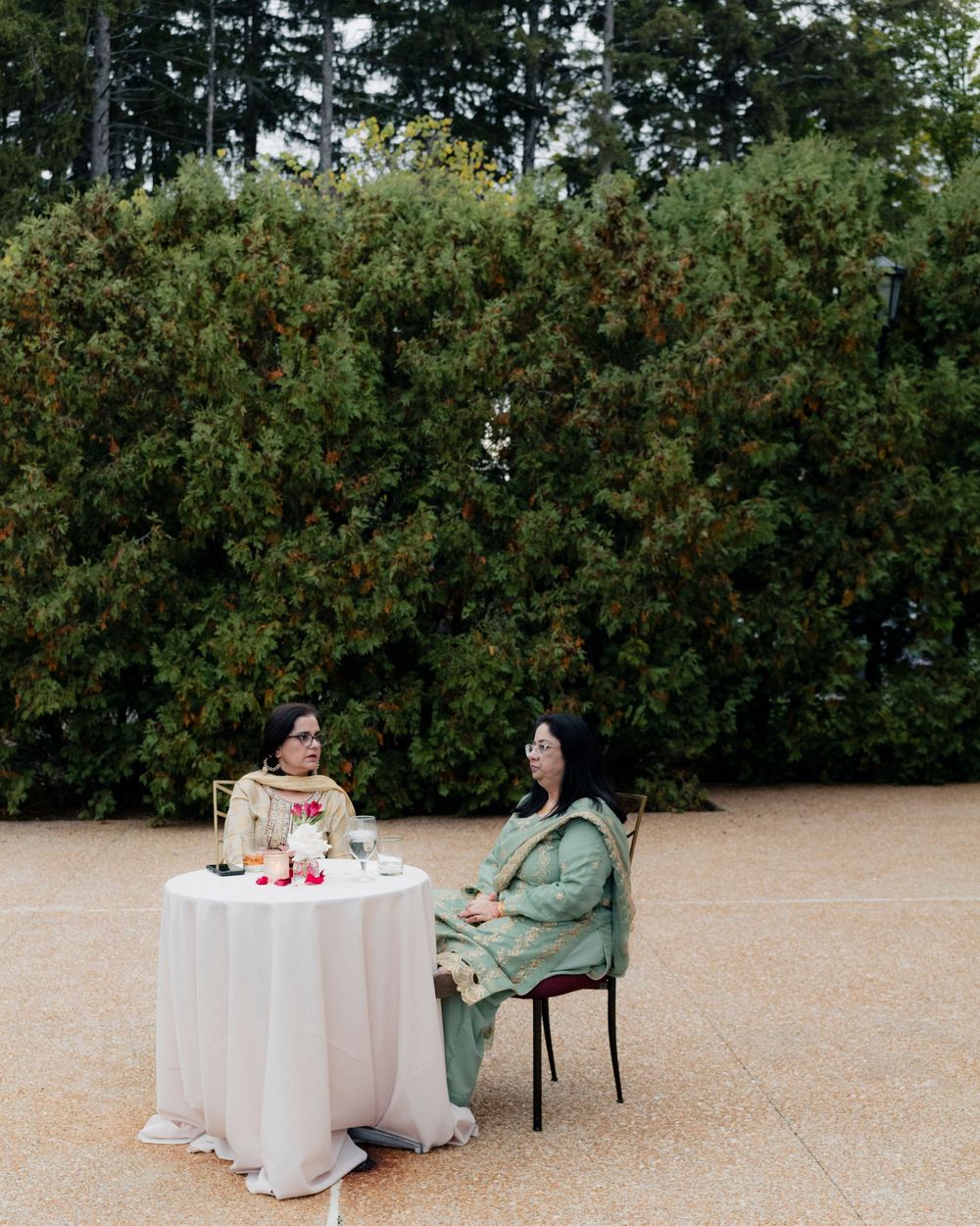 Two guests sit at a table in front of a garden hedge at a Cuneo Mansion Wedding reception.