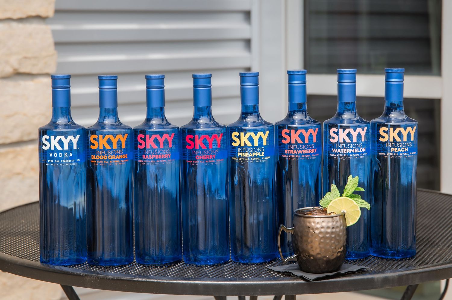 Row of blue SKYY vodka bottles displayed on a shelf with decorative lighting and glass accents.