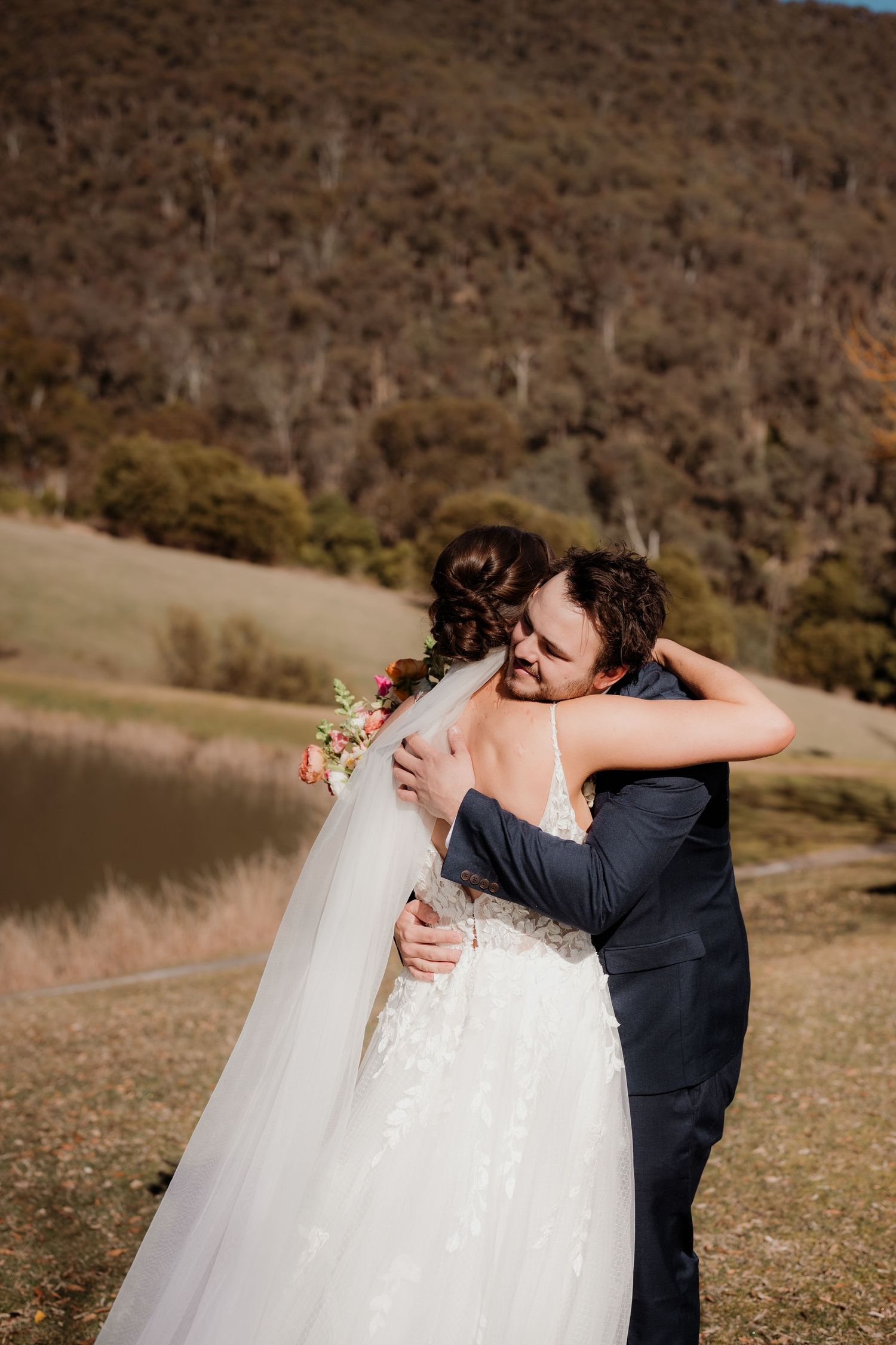 A couple shares an intimate embrace outdoors on their wedding day with mountains and nature in the background.