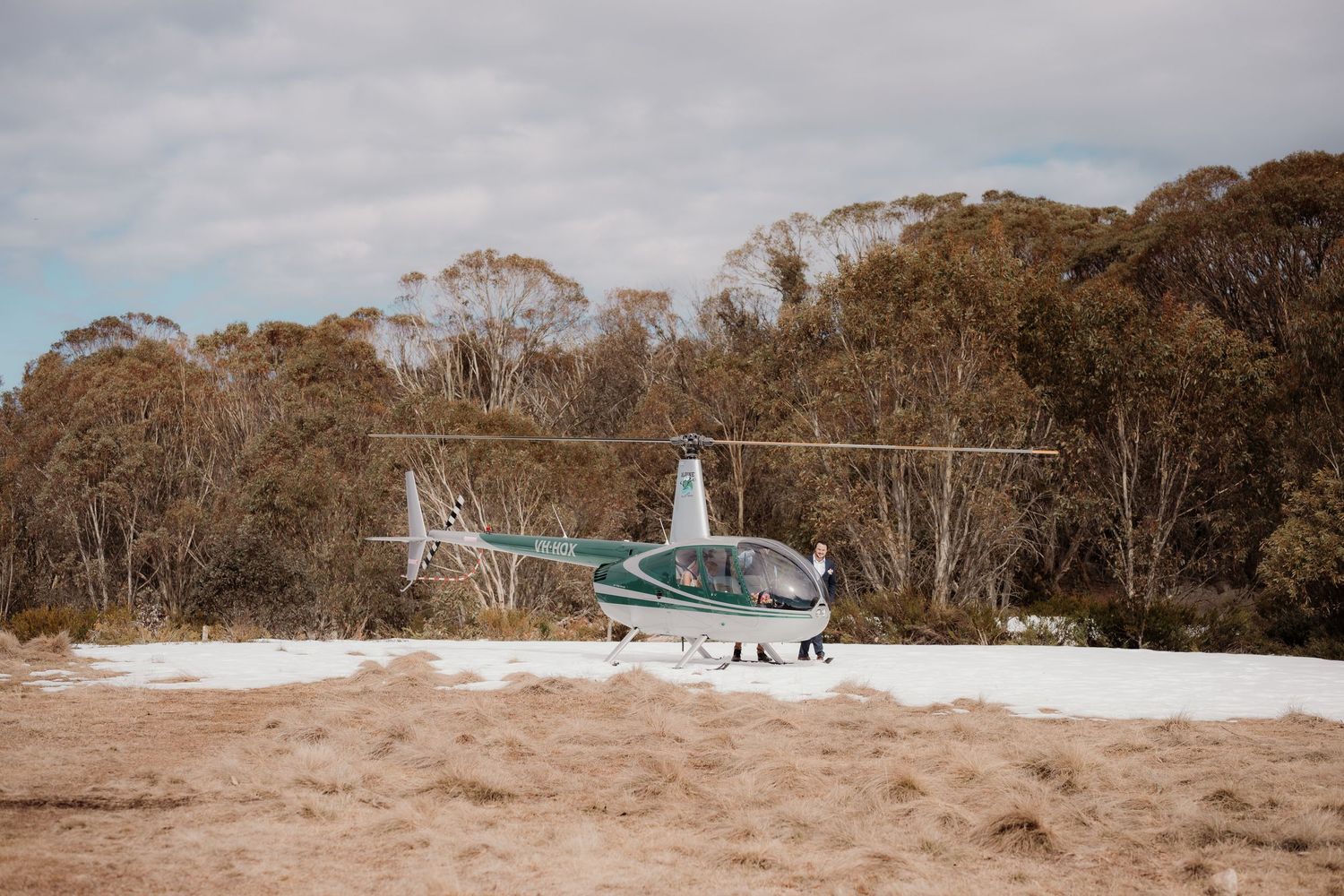Helicopter landing on a dry grassy field near trees during autumn season.