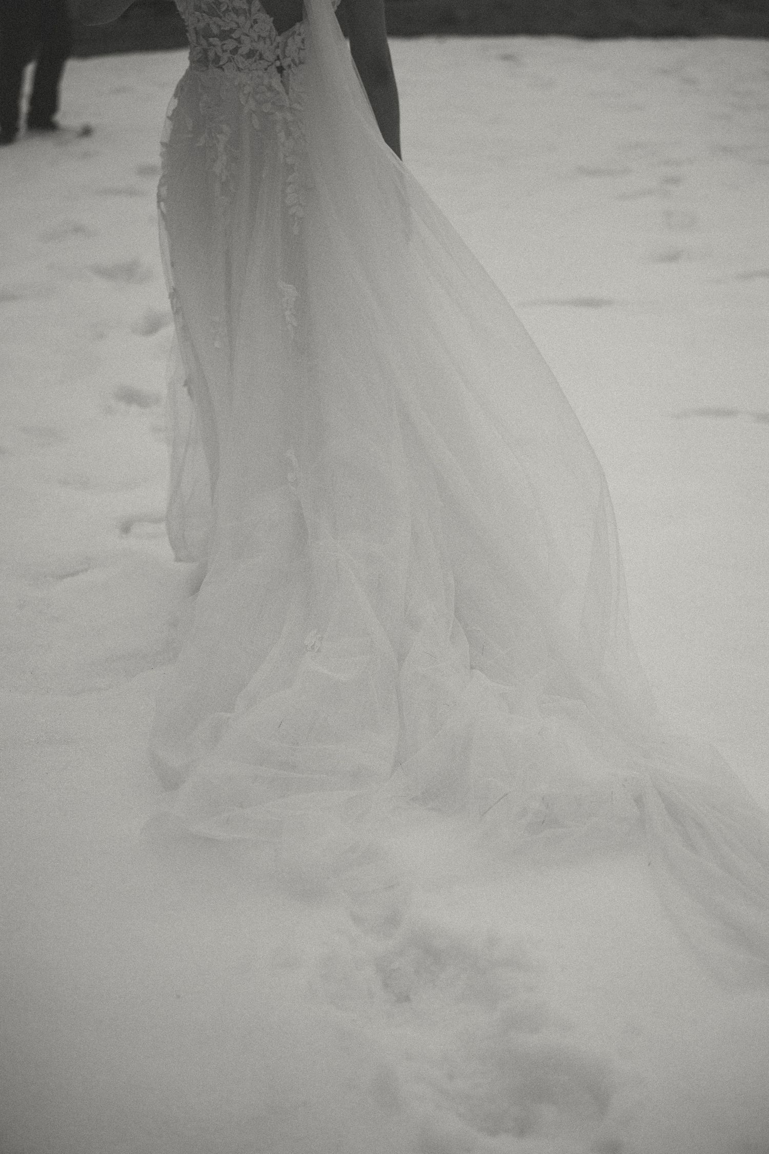 A flowing white wedding dress train with delicate tulle fabric creates an ethereal effect against a light background.