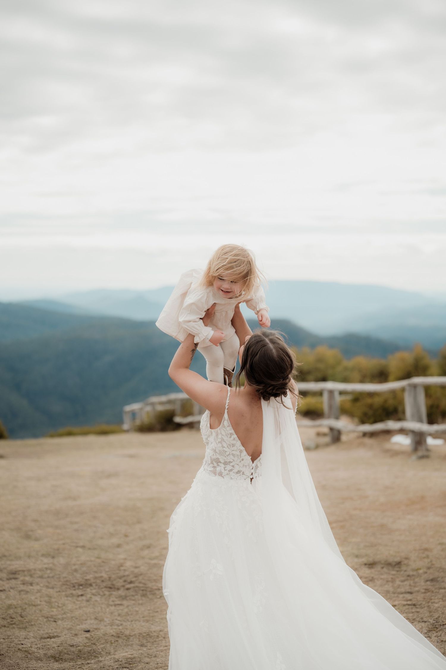 A bride in a flowing white dress dances and twirls on a mountaintop overlook during golden hour.