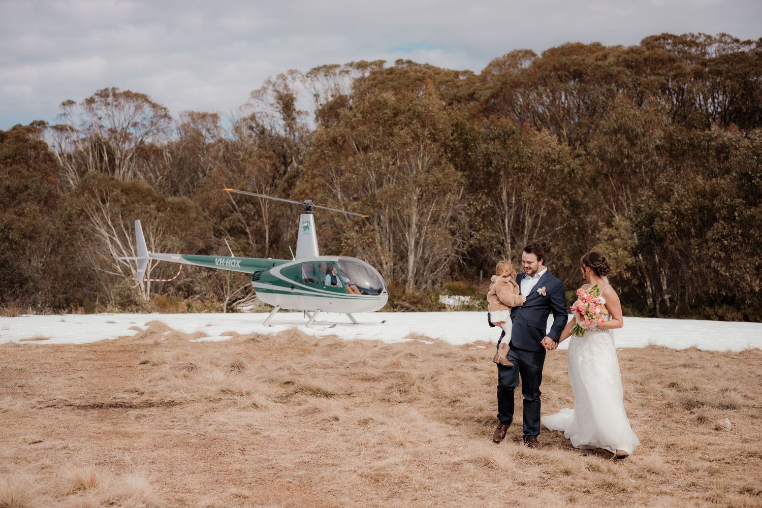 A helicopter lands on a sandy clearing near a wooded area during a wedding photoshoot.