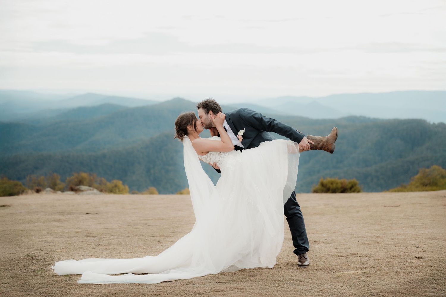 A romantic mountain vista wedding photoshoot shows a couple embracing with dramatic rolling hills in the background.