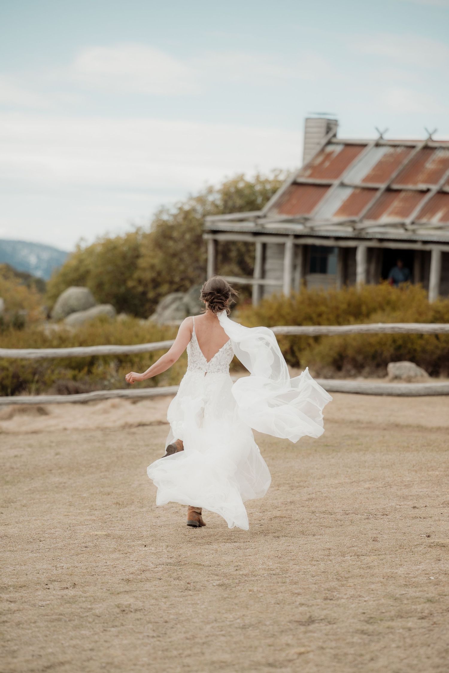 A sequence of photos showing a bride in a flowing white dress twirling and dancing on a sandy beach near rustic buildings.
