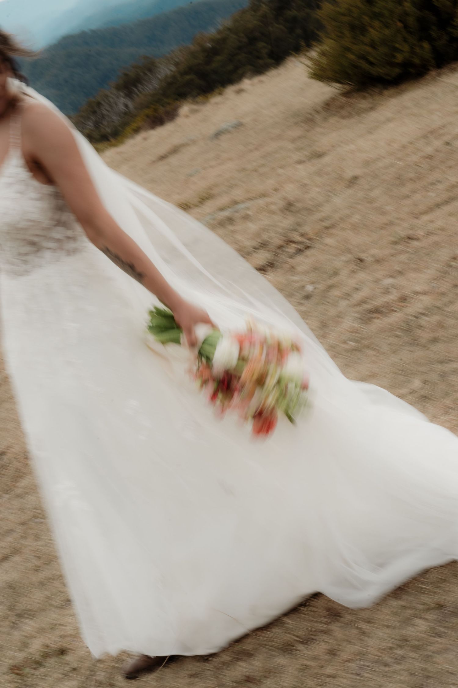 A hand brushes sand off a white wedding dress train on a beach during a photoshoot.