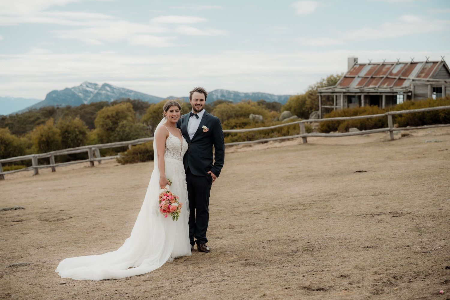 A couple poses for wedding photos in front of majestic mountain landscapes at sunset.