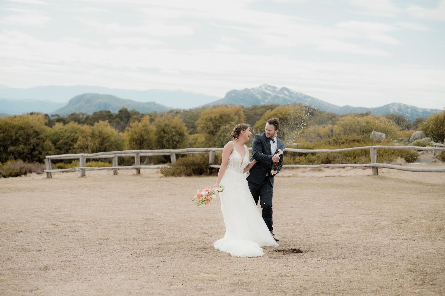 A couple celebrates their wedding day against a scenic desert mountain backdrop at sunset.