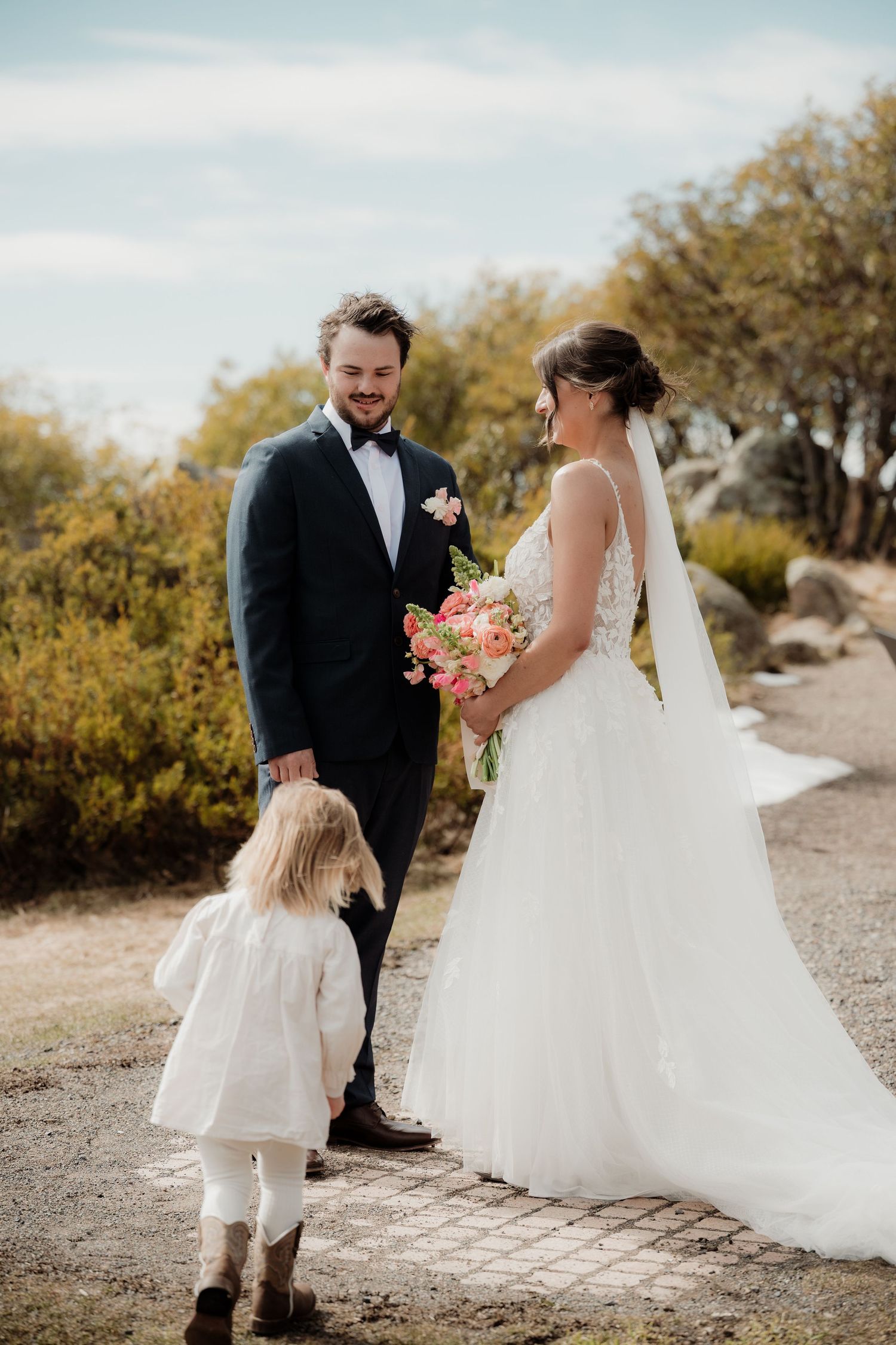 A series of wedding photos showing a bride in a white gown and groom in a black suit with a flower girl on a gravel path.