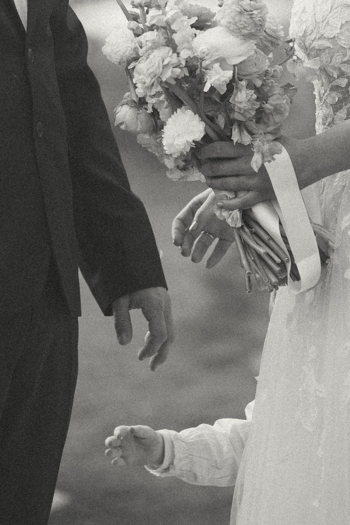 A black and white close-up photo of hands holding an elegant white bridal bouquet during a wedding ceremony.